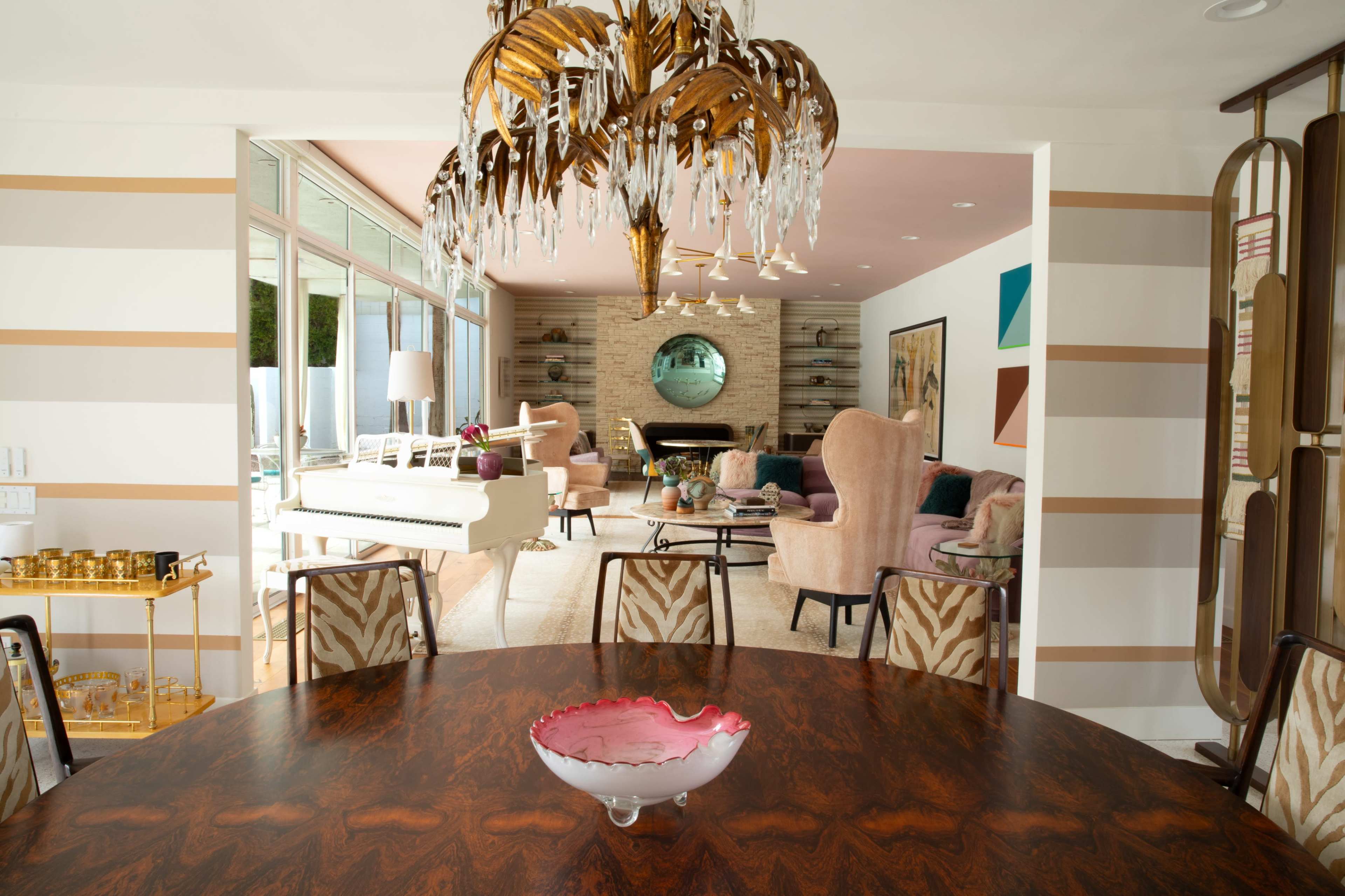 The image shows a stylish interior space with a dining table at the forefront, leading into a living area featuring elegant furniture and modern decor.