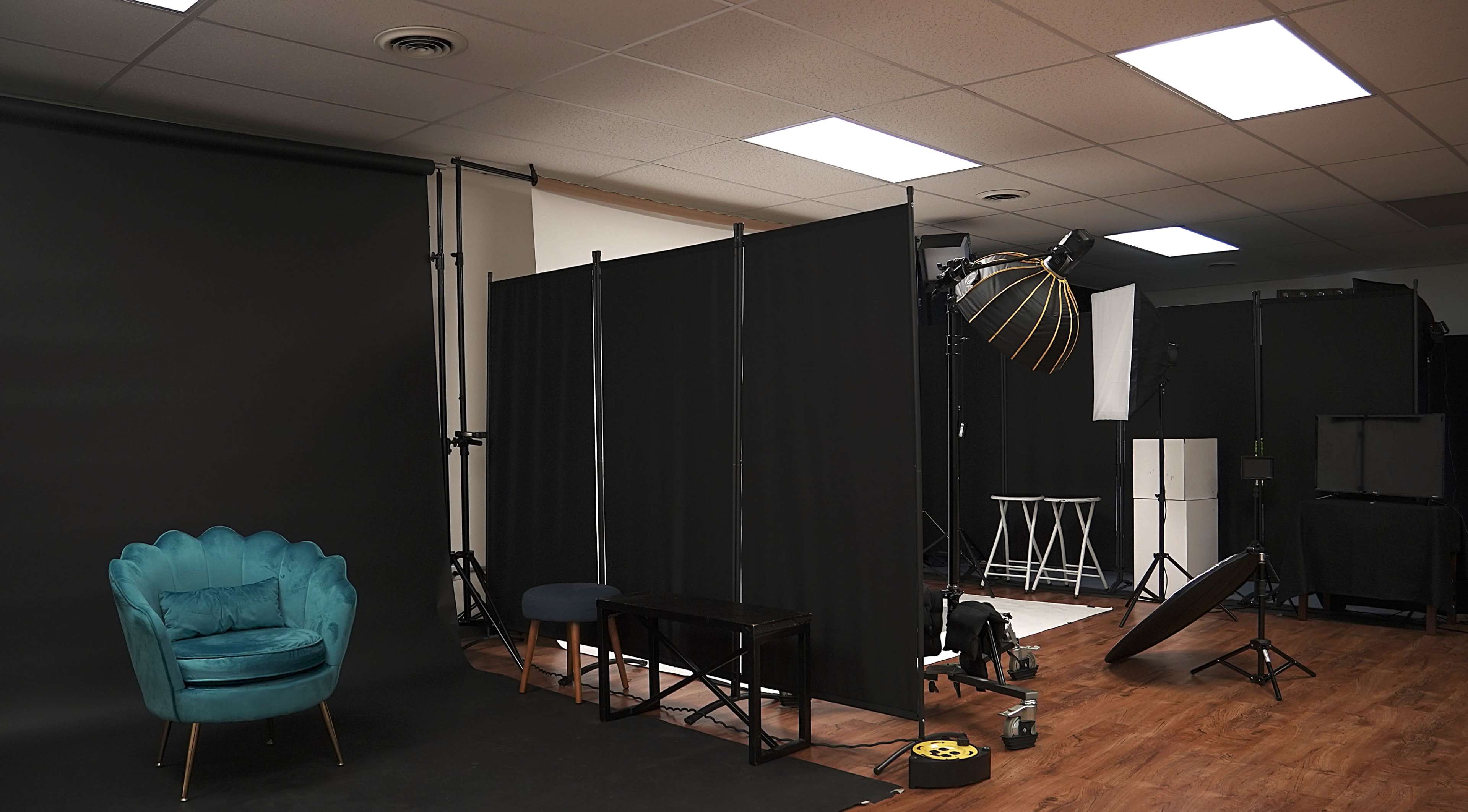 A photography studio is set up with backdrops, lighting equipment, and furniture, including a teal chair and a wooden bench.