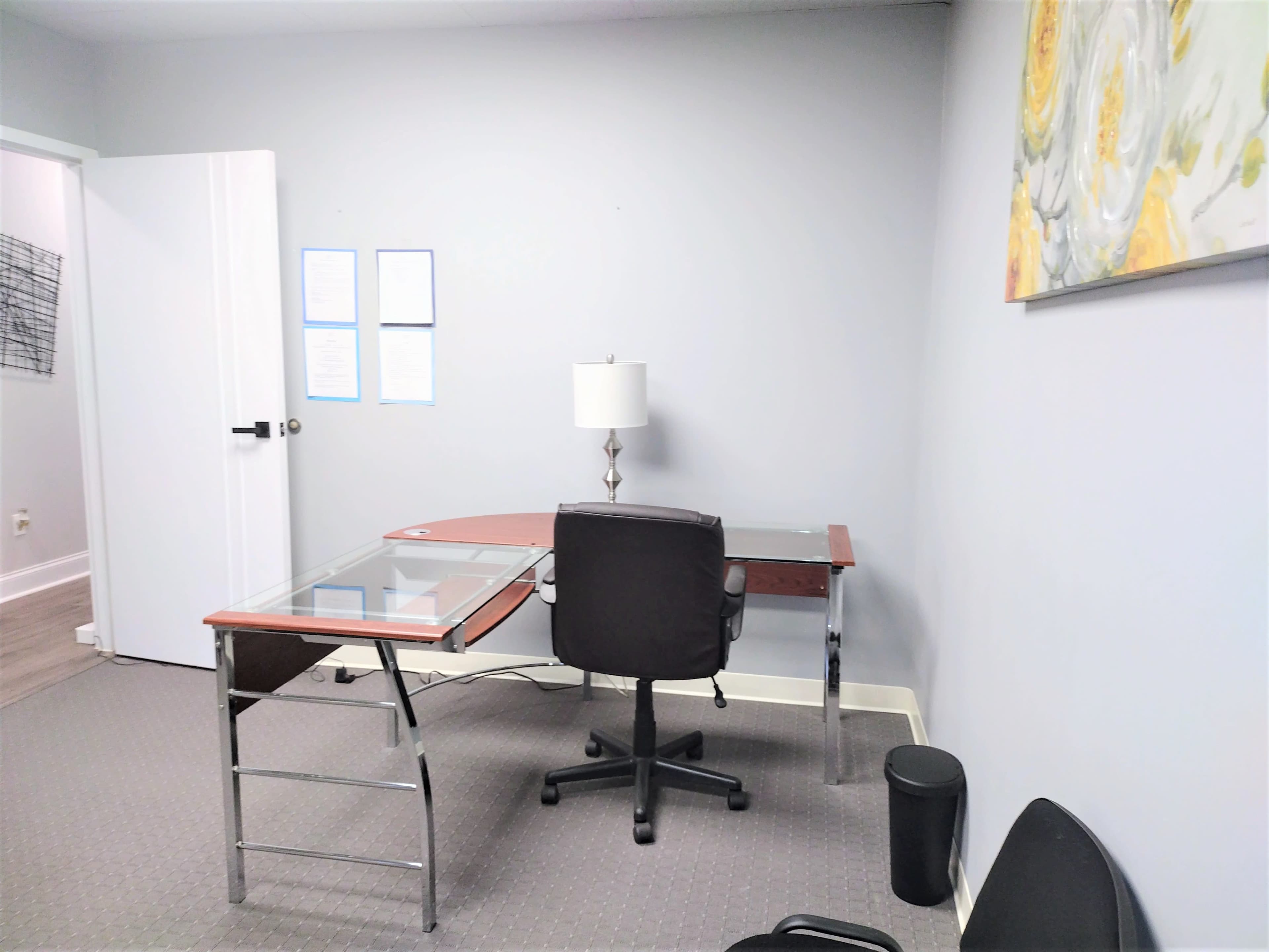 A small office space with a modern desk, a chair, a lamp, and a piece of wall art.
