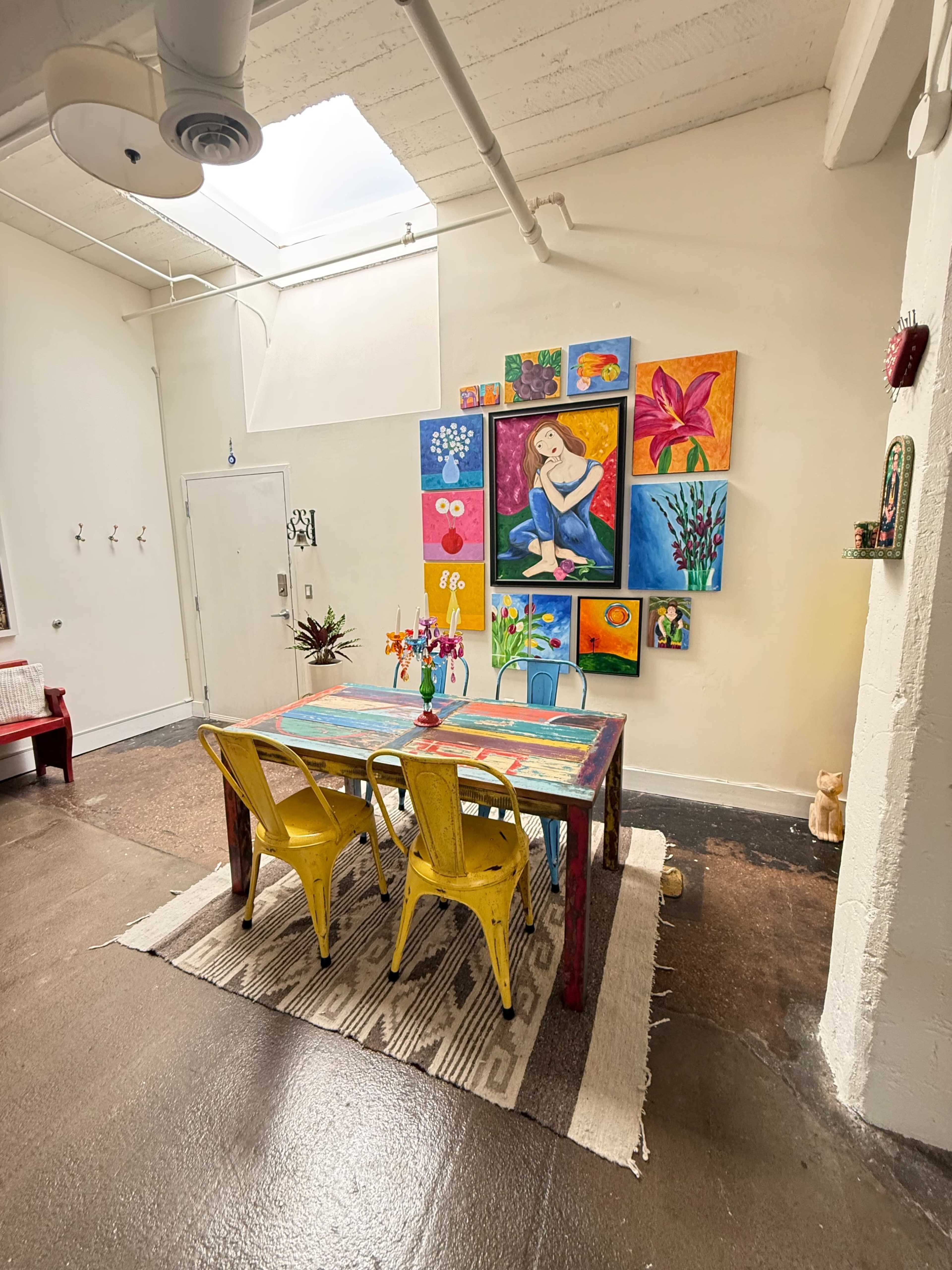 A brightly colored table with yellow chairs is set in a room decorated with vibrant artwork on the wall.