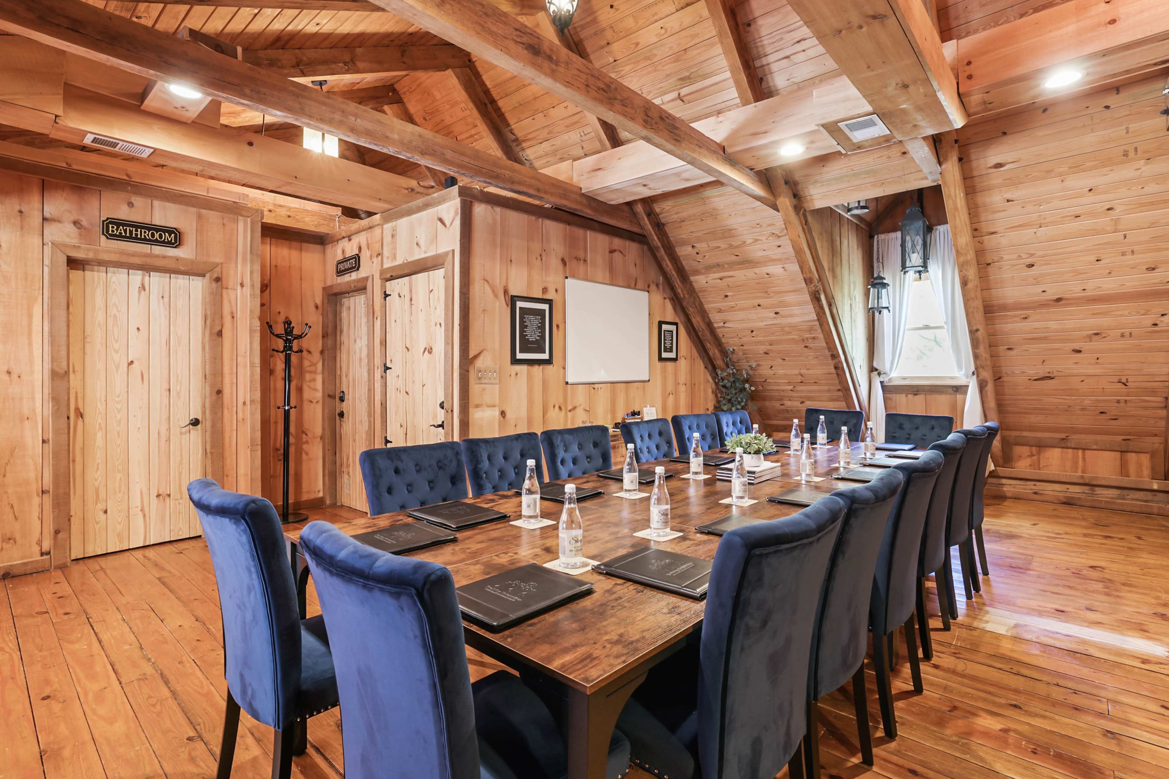 A large meeting room features a long wooden table surrounded by blue chairs, with wooden beams and walls creating a rustic atmosphere.