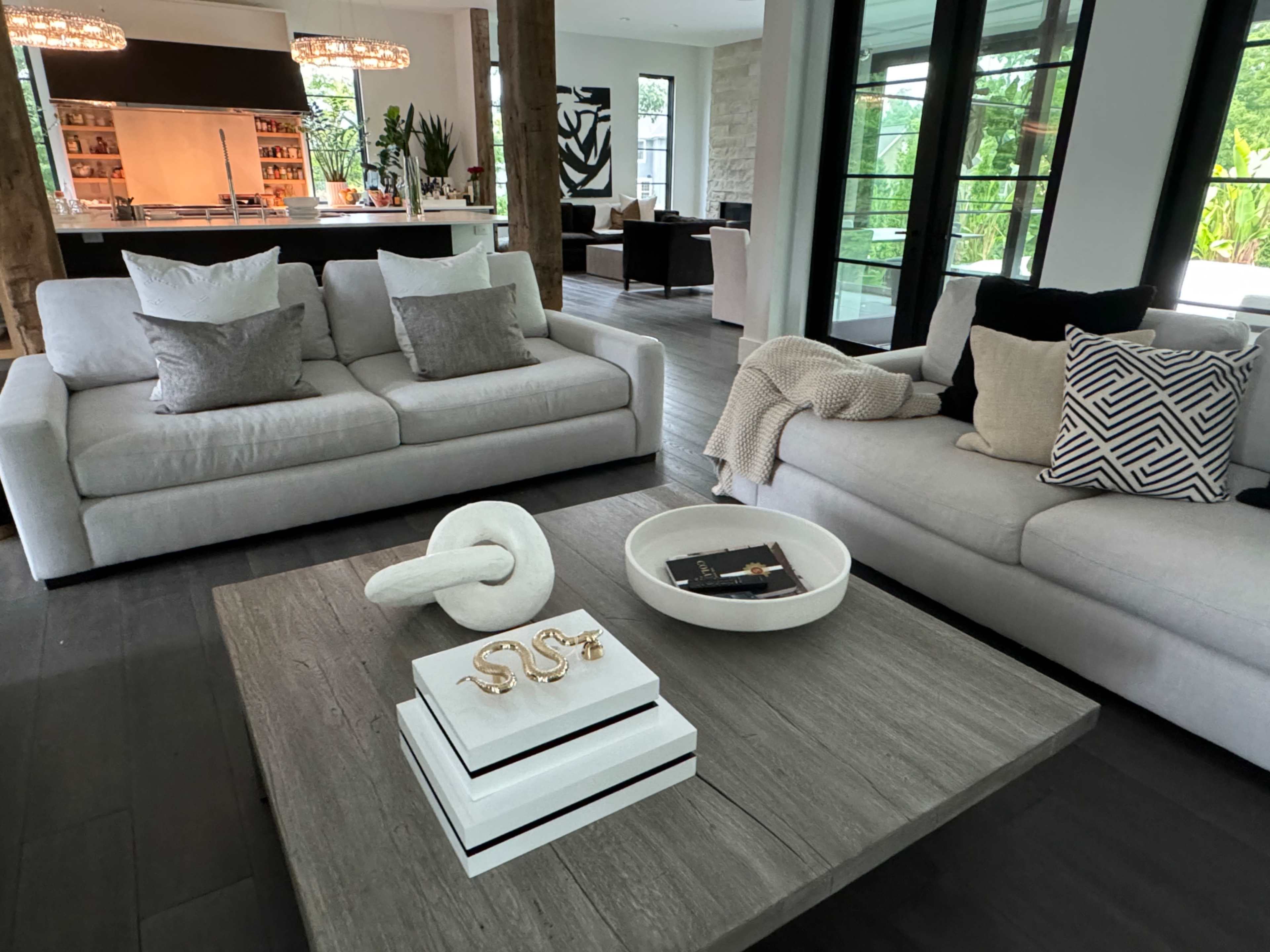 A modern living room featuring two light gray sofas with a textured throw blanket and decorative pillows around a dark wooden coffee table.