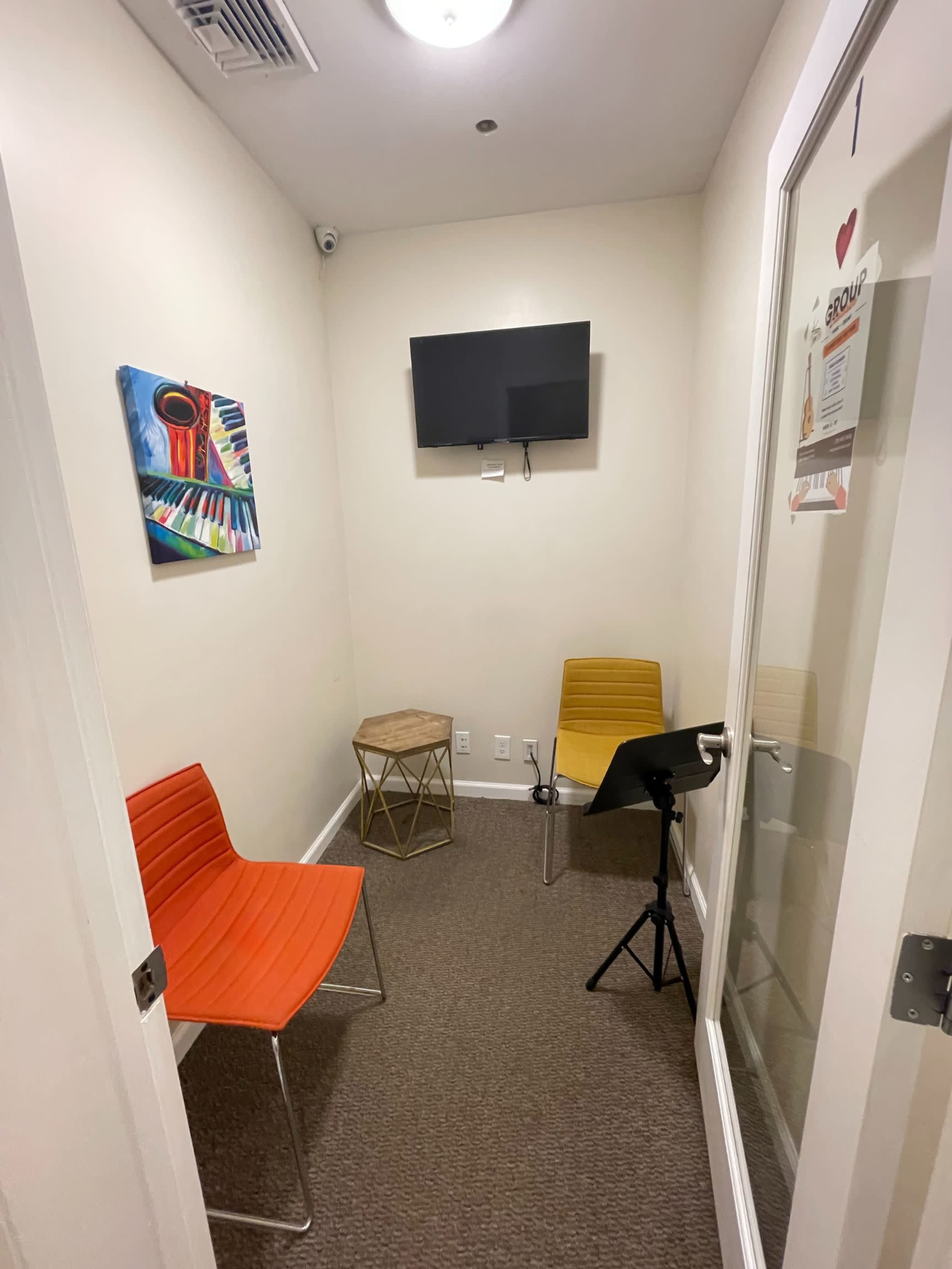 A small room with two chairs, a table, a wall-mounted television, and a colorful painting on the wall.
