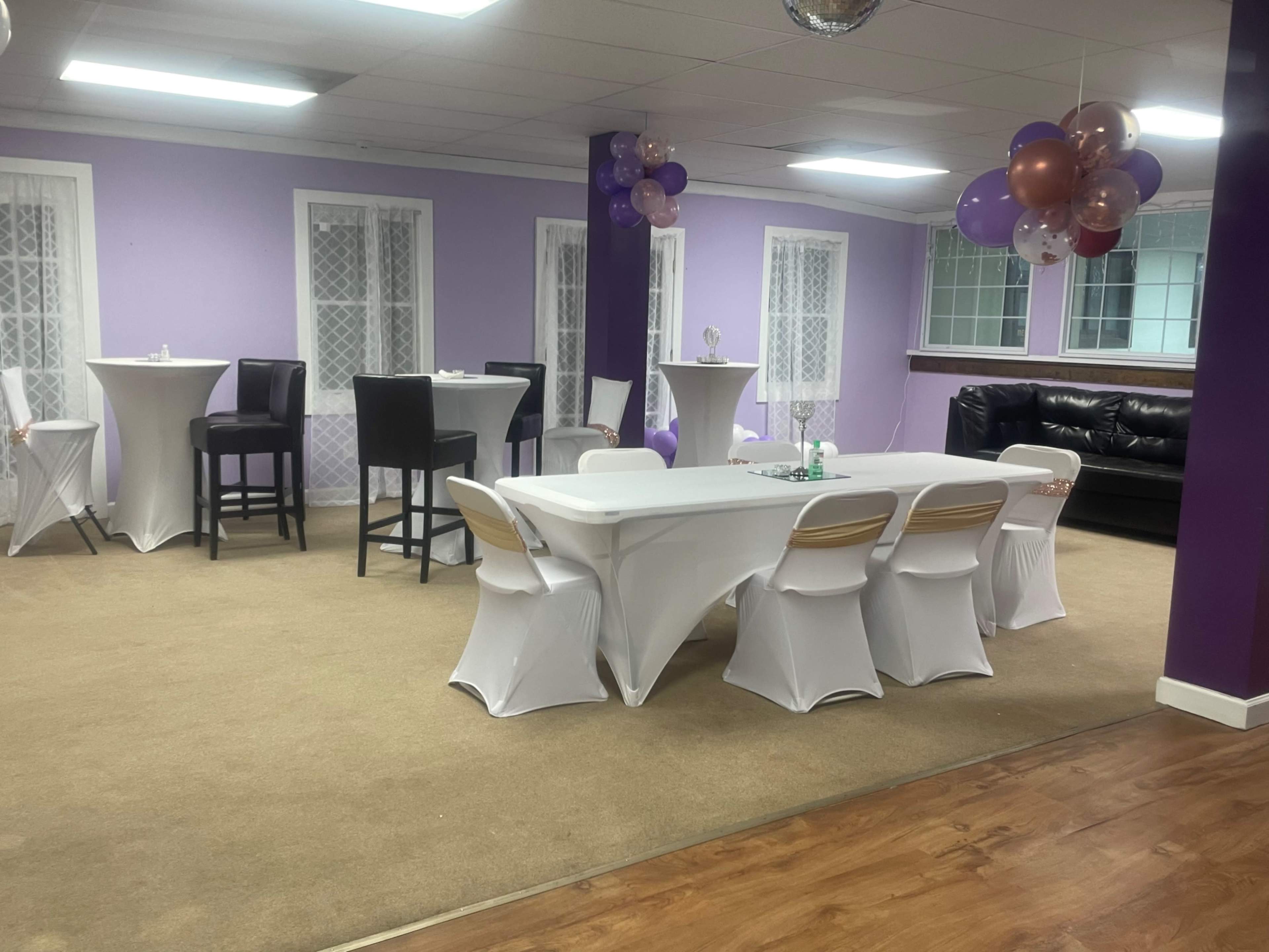A party venue with purple walls, tables covered in white tablecloths, and decorative balloons in the corner.