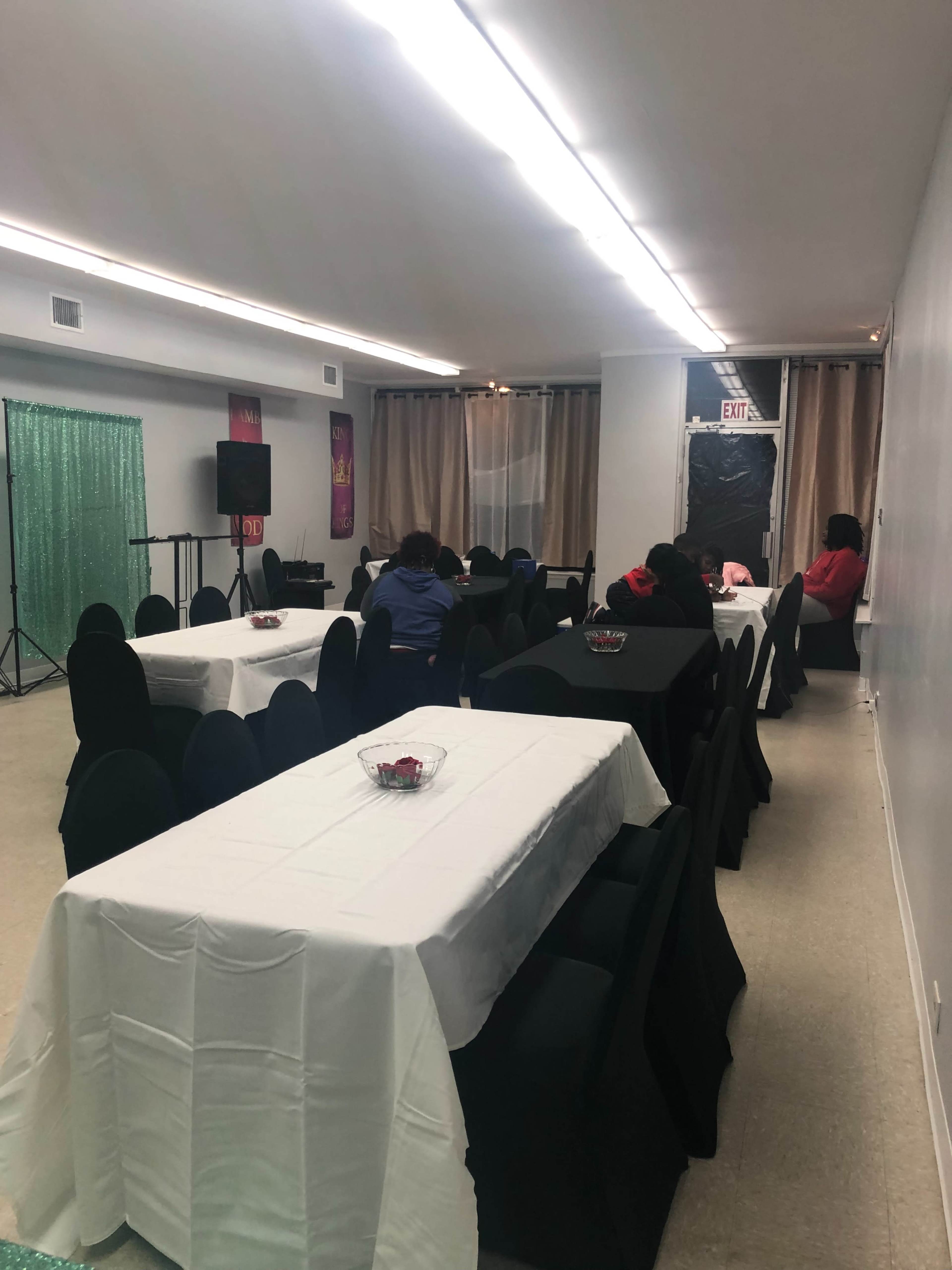The image shows an indoor event space with multiple tables covered in black and white tablecloths, and several people seated at the tables.