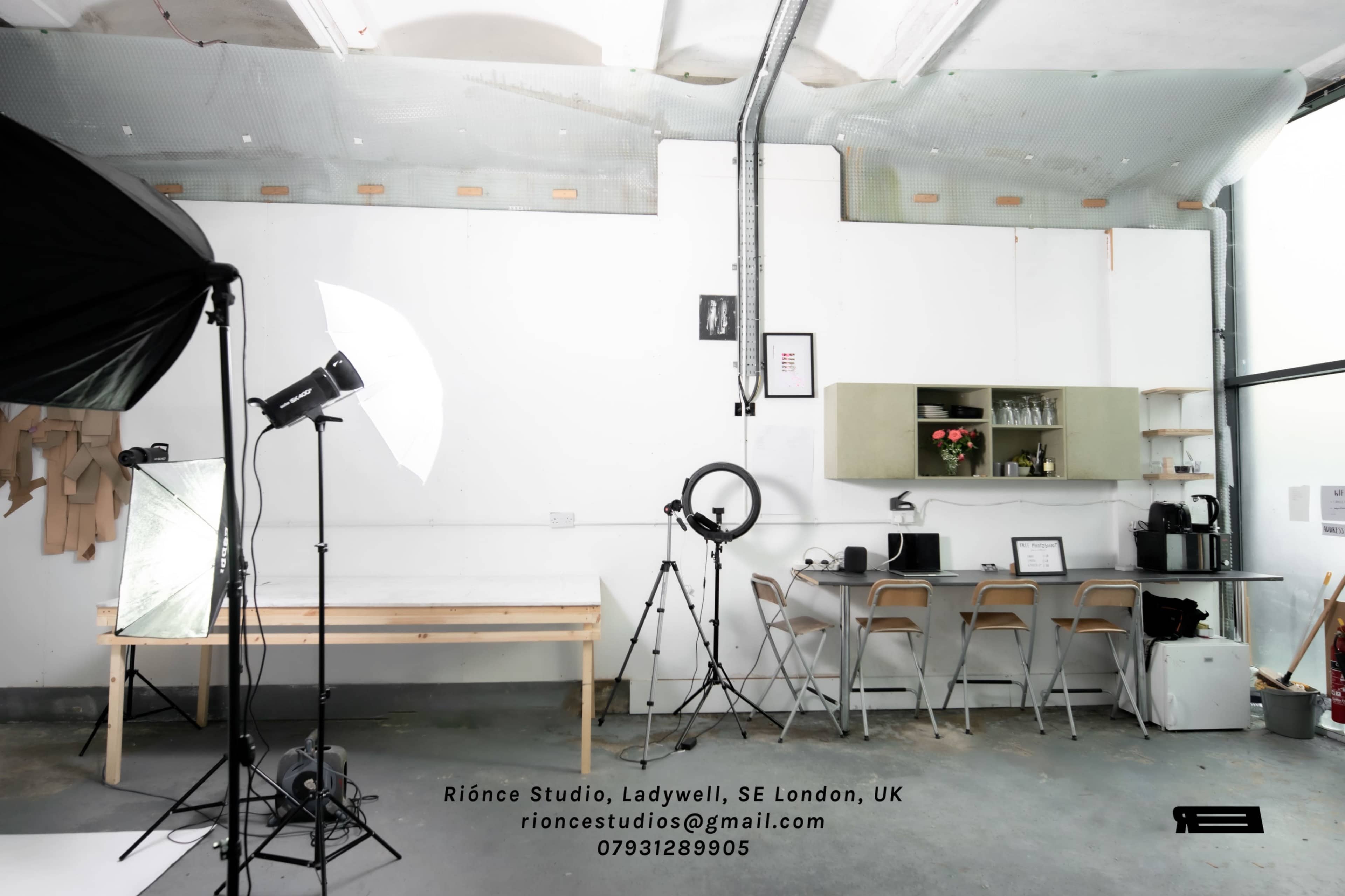 A well-lit studio space in London with a minimalist design, featuring a kitchen area, a photography light setup, and a worktable.