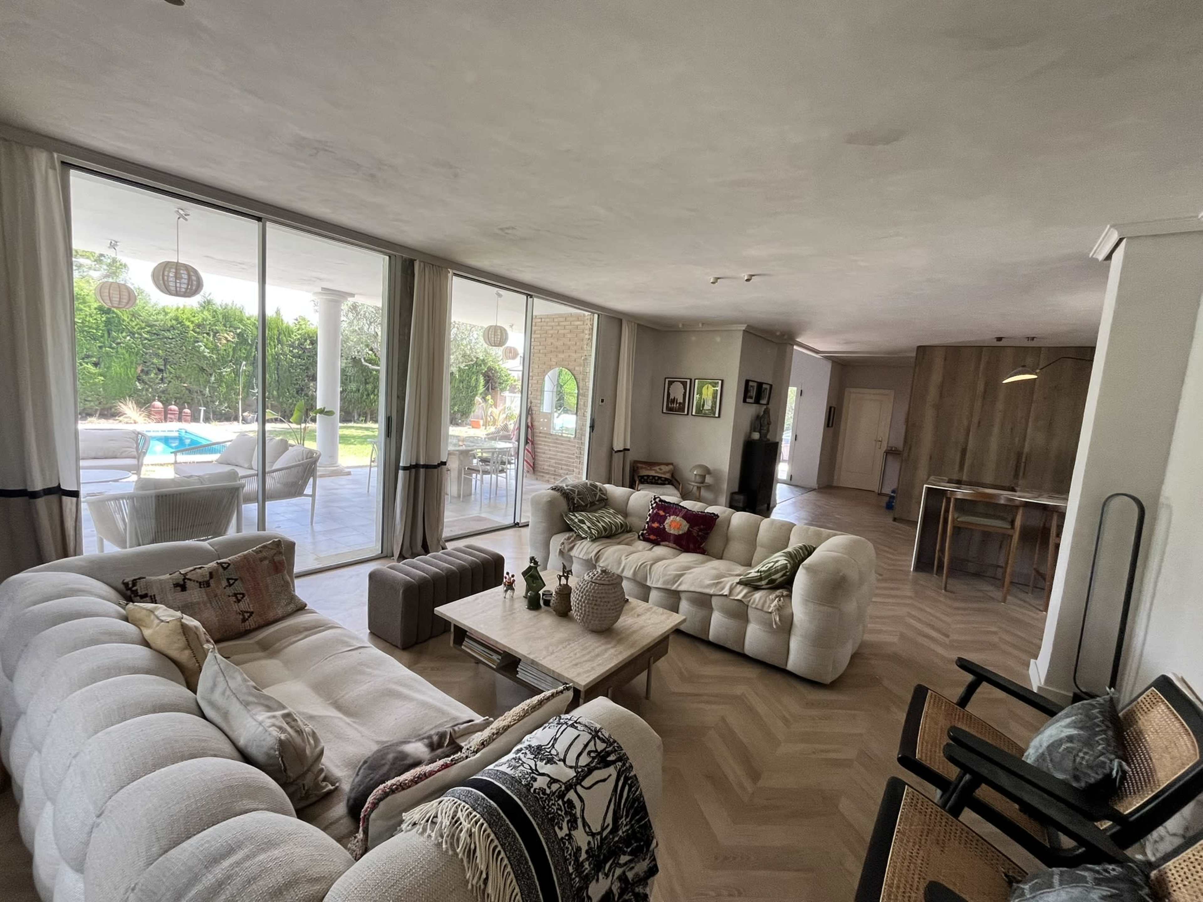 The image shows a spacious living room with two large sofas, a wooden coffee table, and a view of a well-lit patio and garden through glass doors.