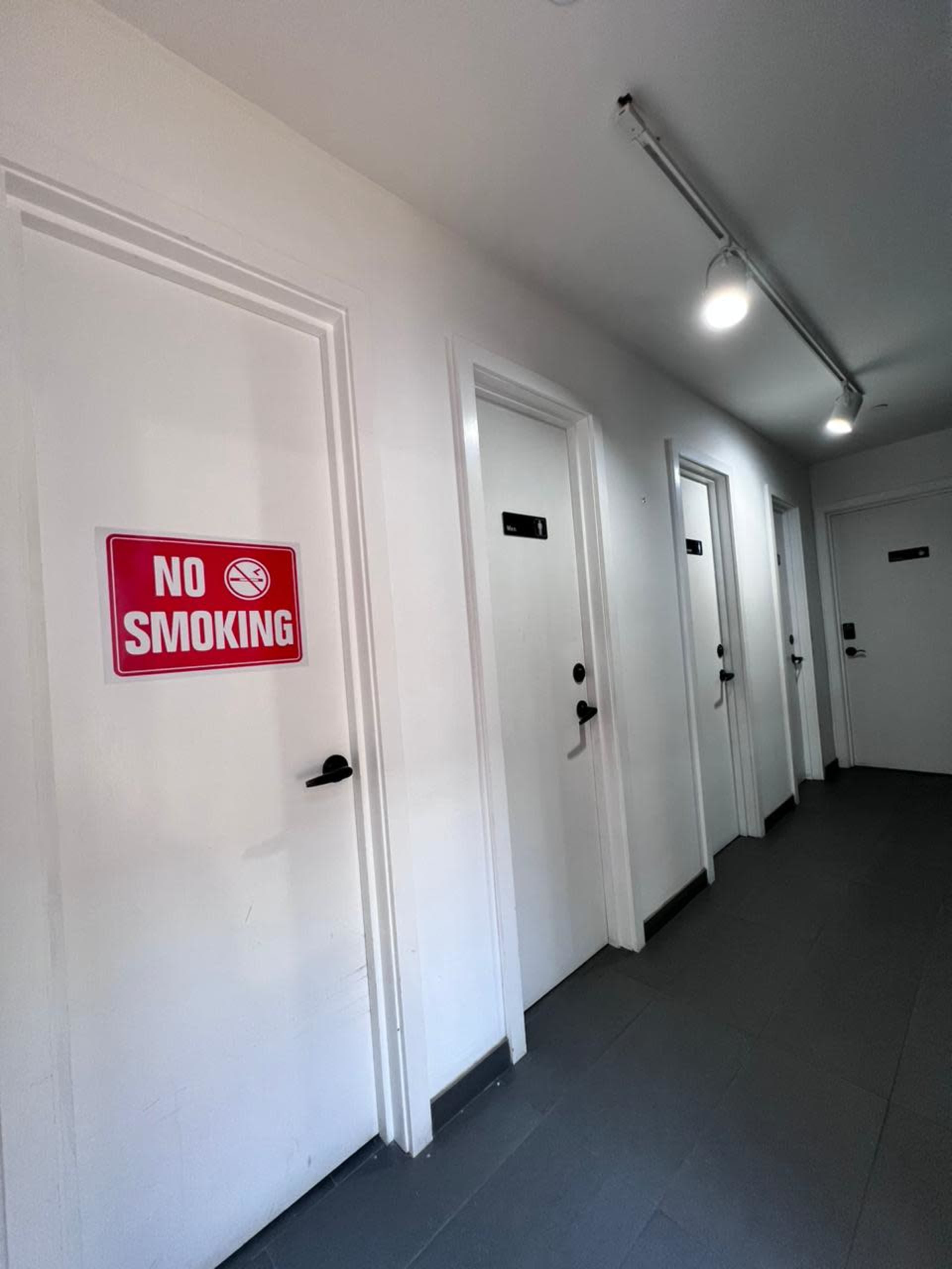 The image shows a hallway with several doors, one of which has a "NO SMOKING" sign prominently displayed.