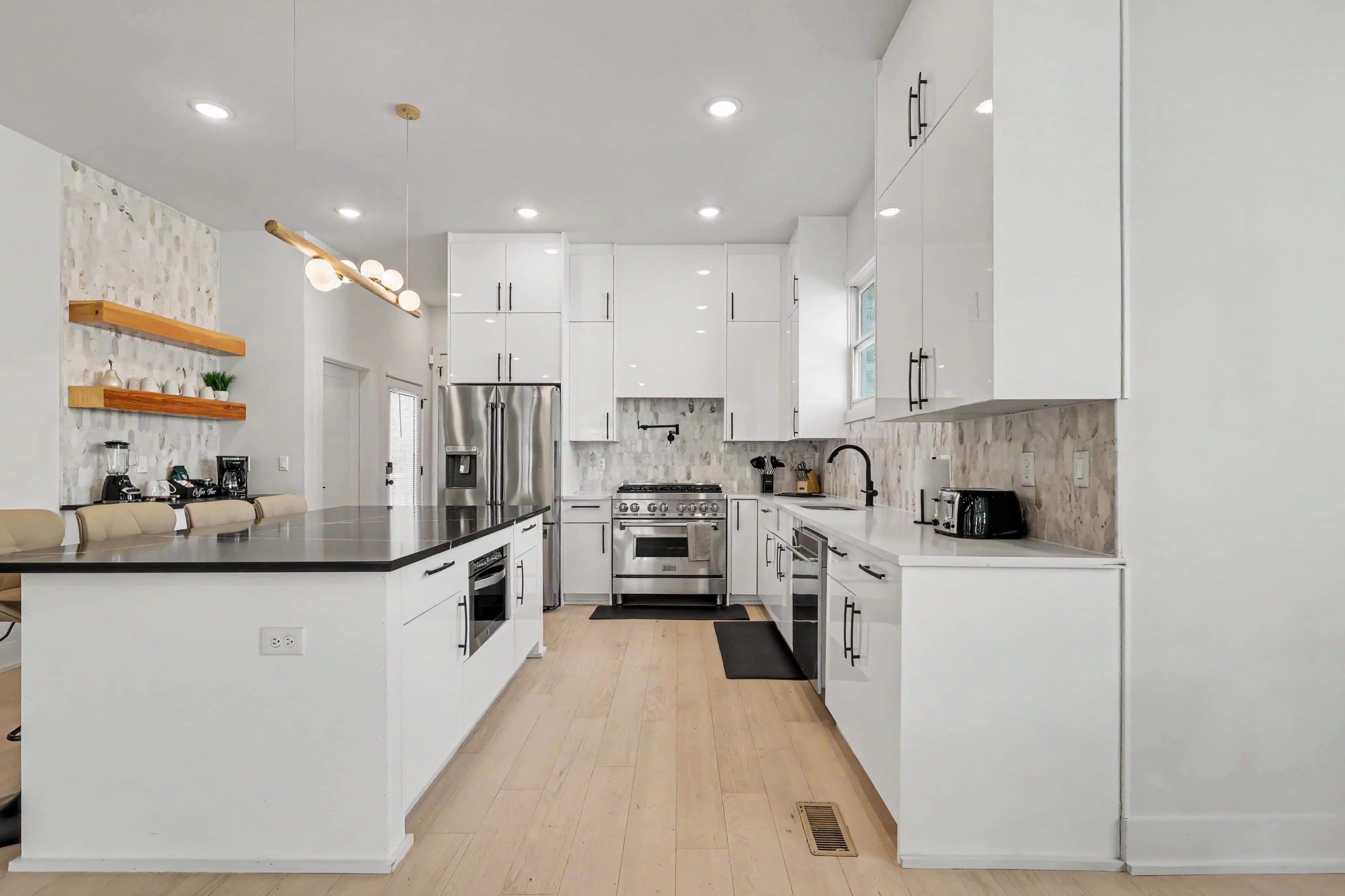 The image shows a modern kitchen featuring white cabinets, stainless steel appliances, and a large island with a black countertop.