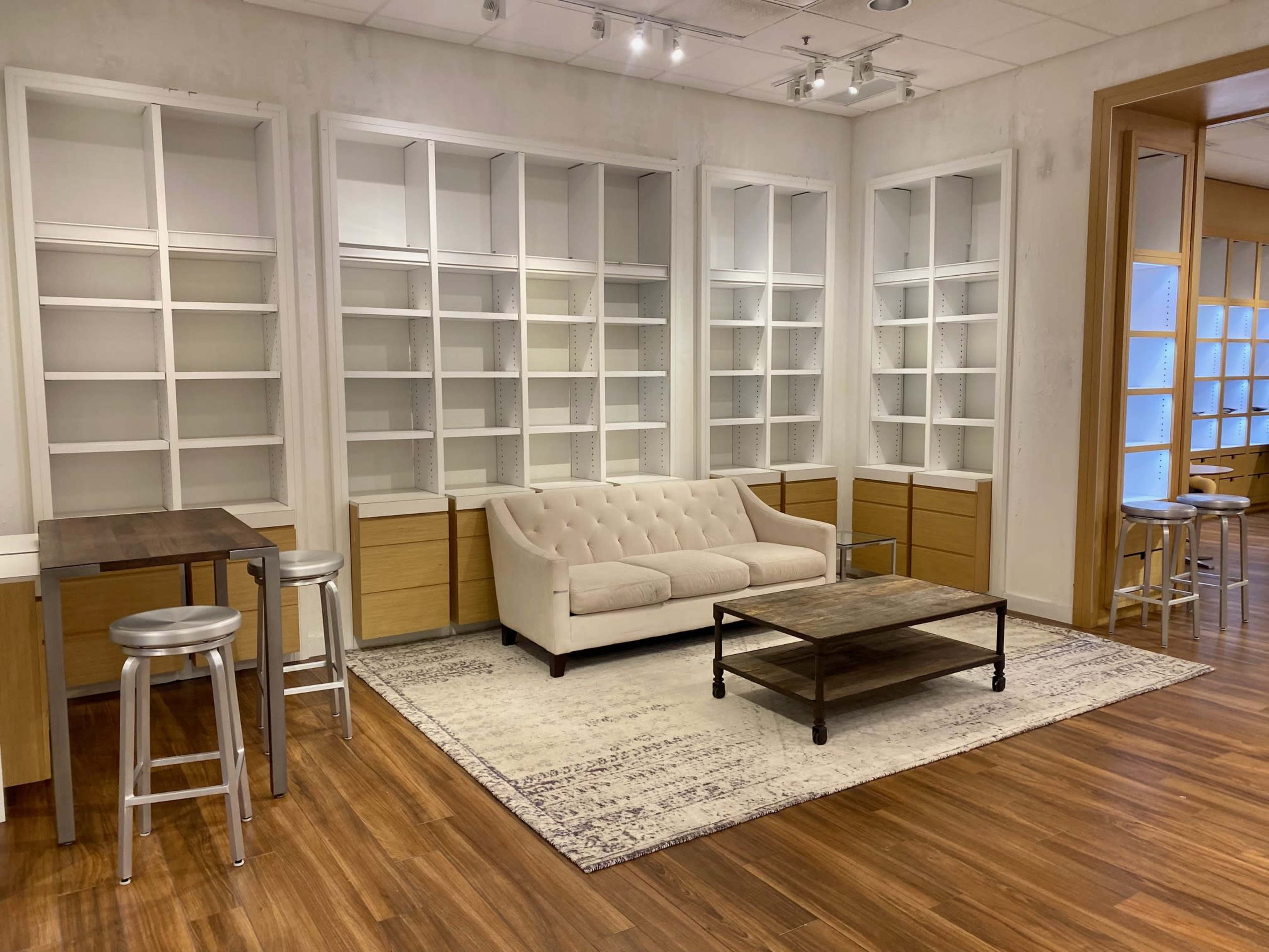 A modern room with a beige couch, a coffee table, and built-in shelving units, along with tall stools and small tables on a wooden floor.