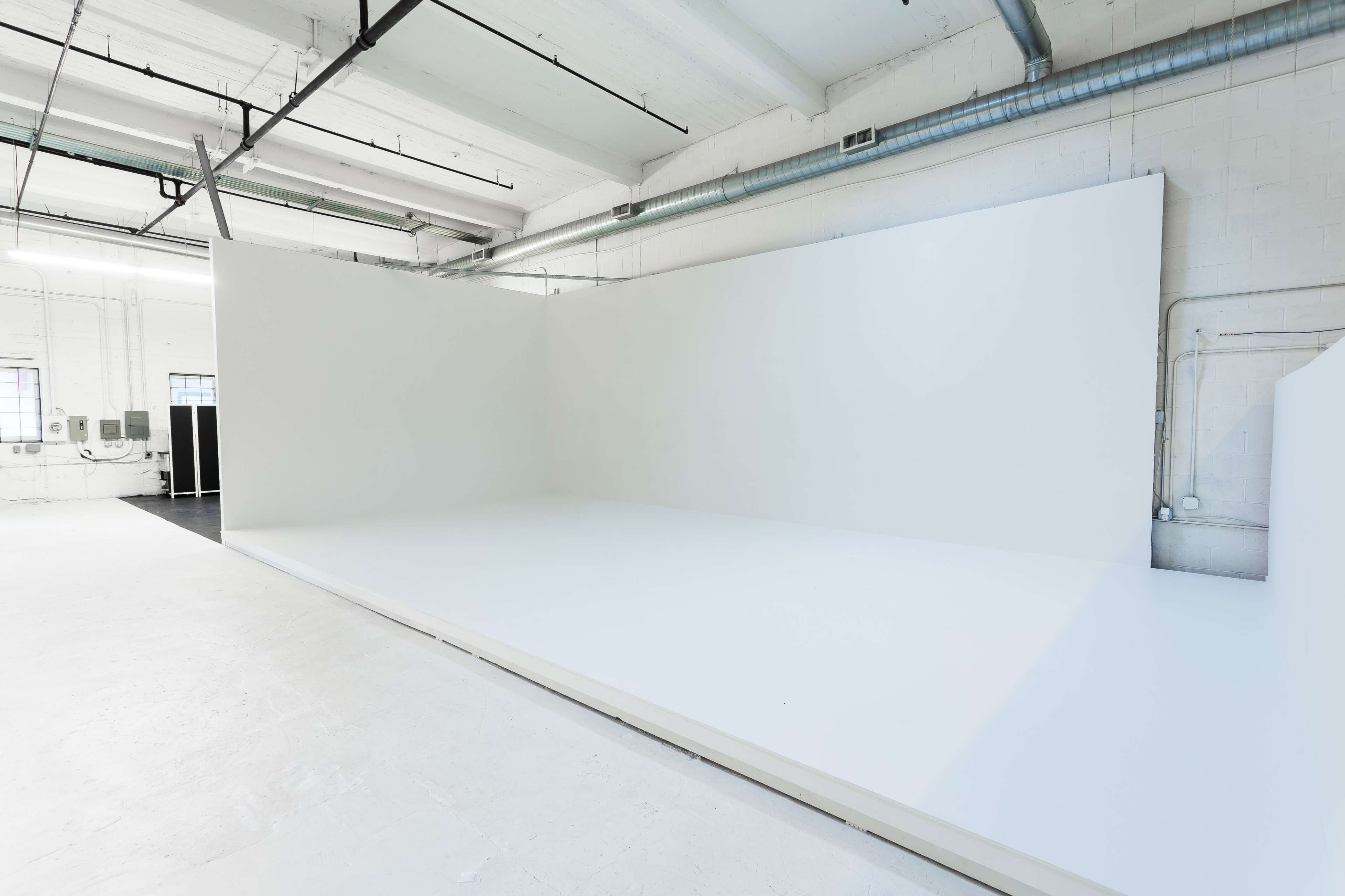A spacious, empty studio with white walls and a white floor, illuminated by overhead lights.