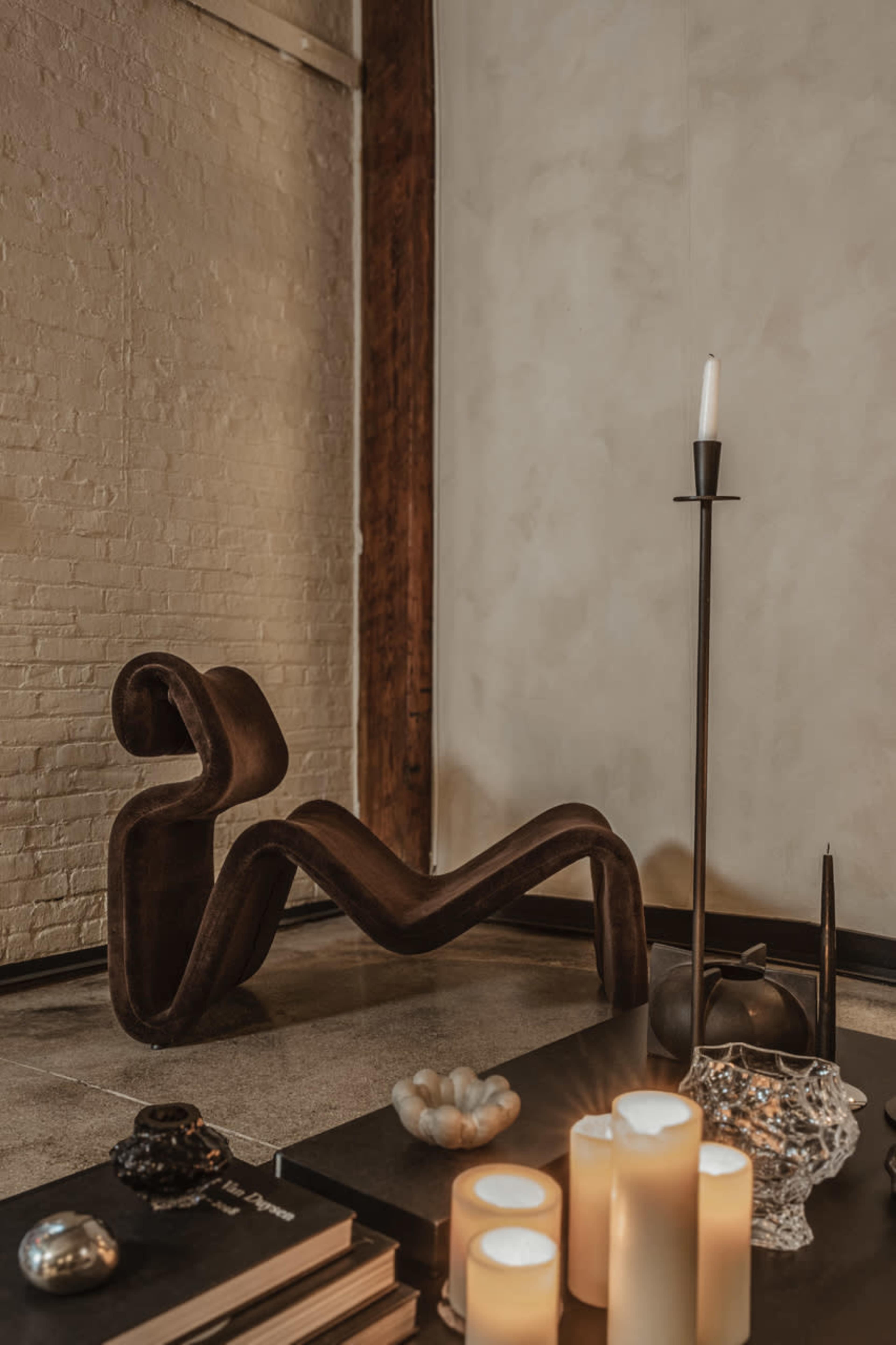 A modern brown chair in a minimalist setting, accompanied by decorative candles and various objects on a table.