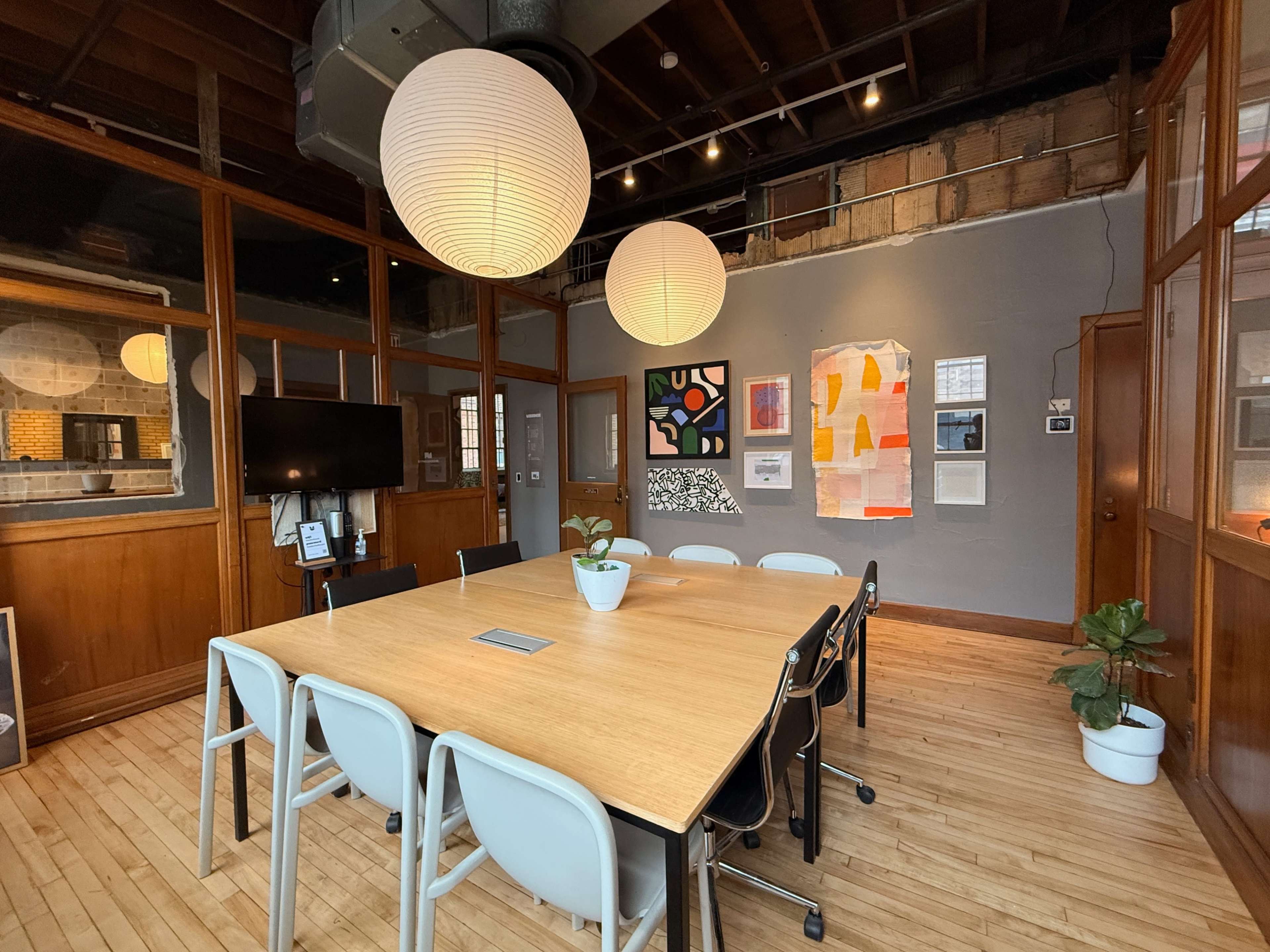 The image shows a modern meeting room featuring a large wooden table surrounded by white chairs, with a backdrop of wooden paneling and decorative lighting.