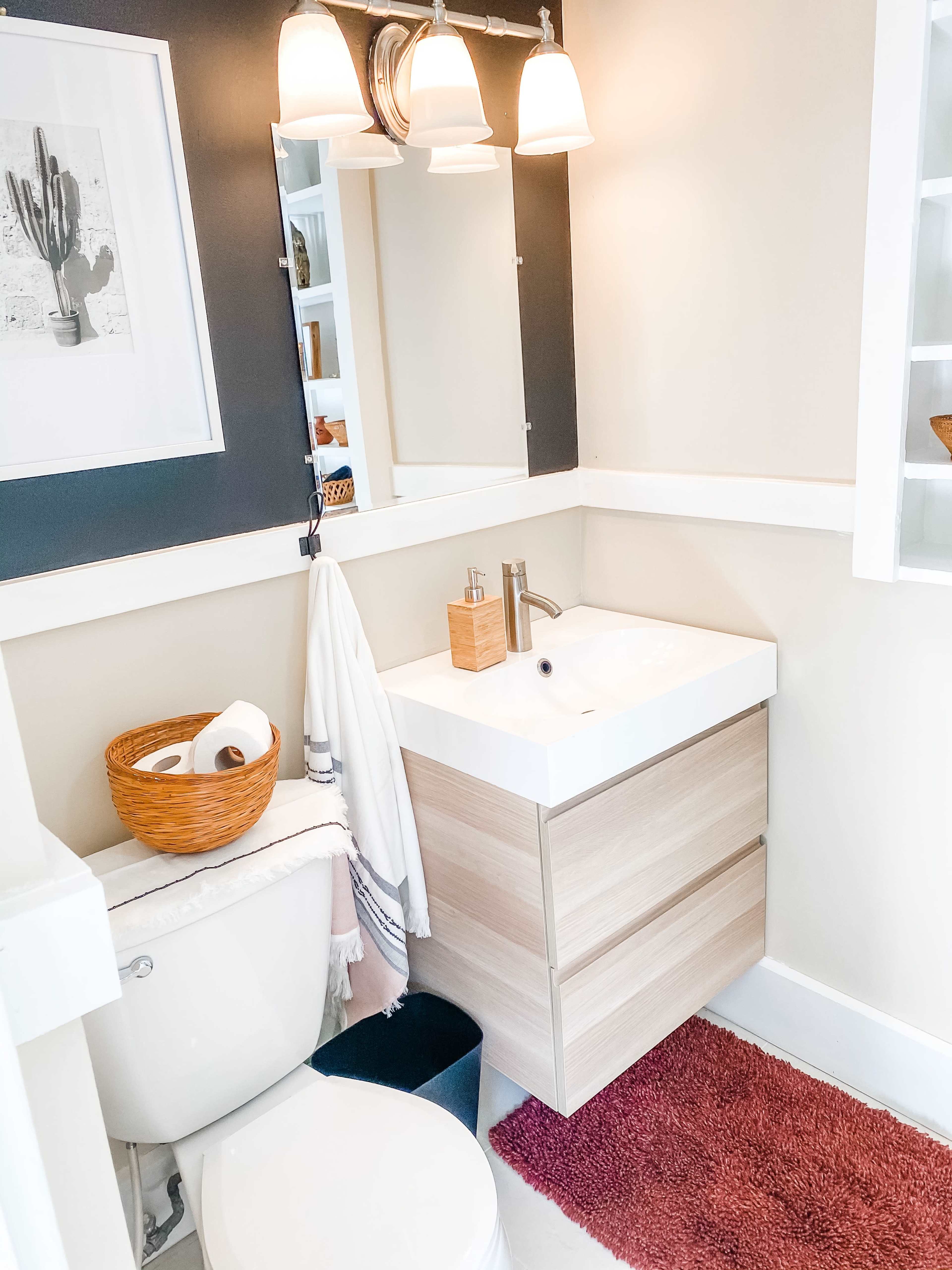 A compact bathroom features a wall-mounted sink with wooden drawers, a toilet, a towel hanging nearby, and a round mirror above the sink.