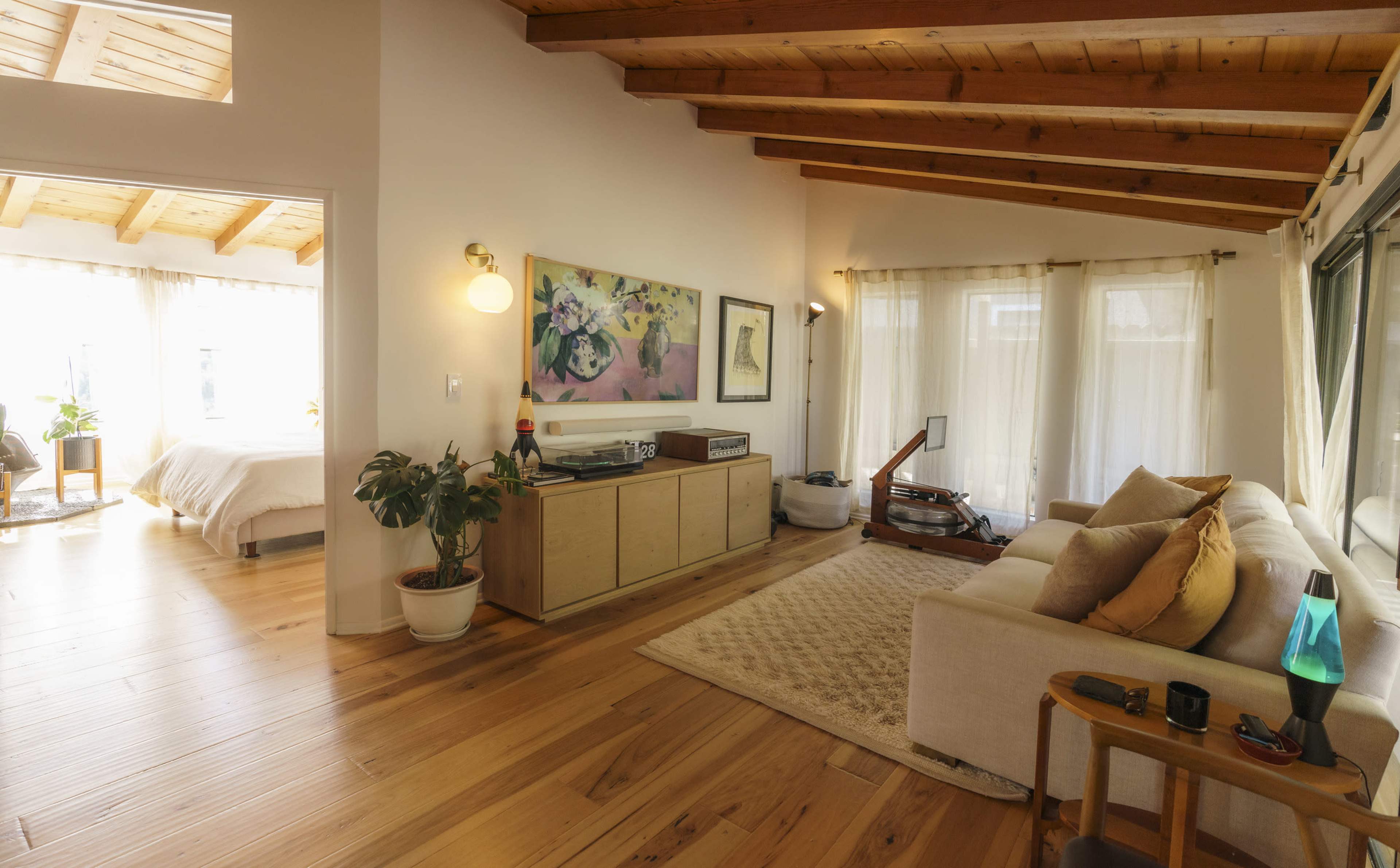 A bright, open-concept living space with wooden beams, a sofa, a vinyl record player, and large windows letting in natural light.