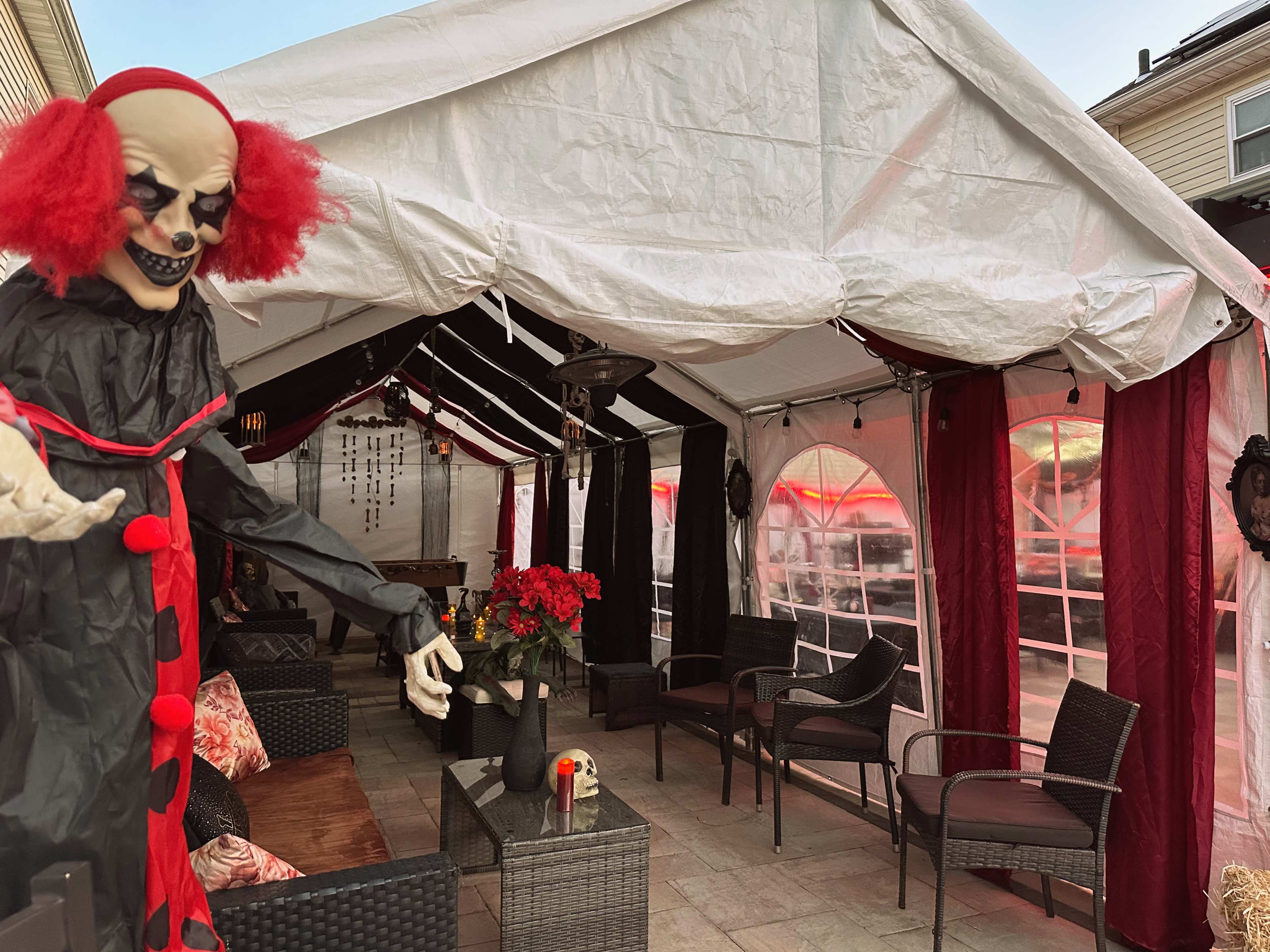 A Halloween-themed tent is set up, featuring dark decorations, a large clown figure, seating areas, and red accents.