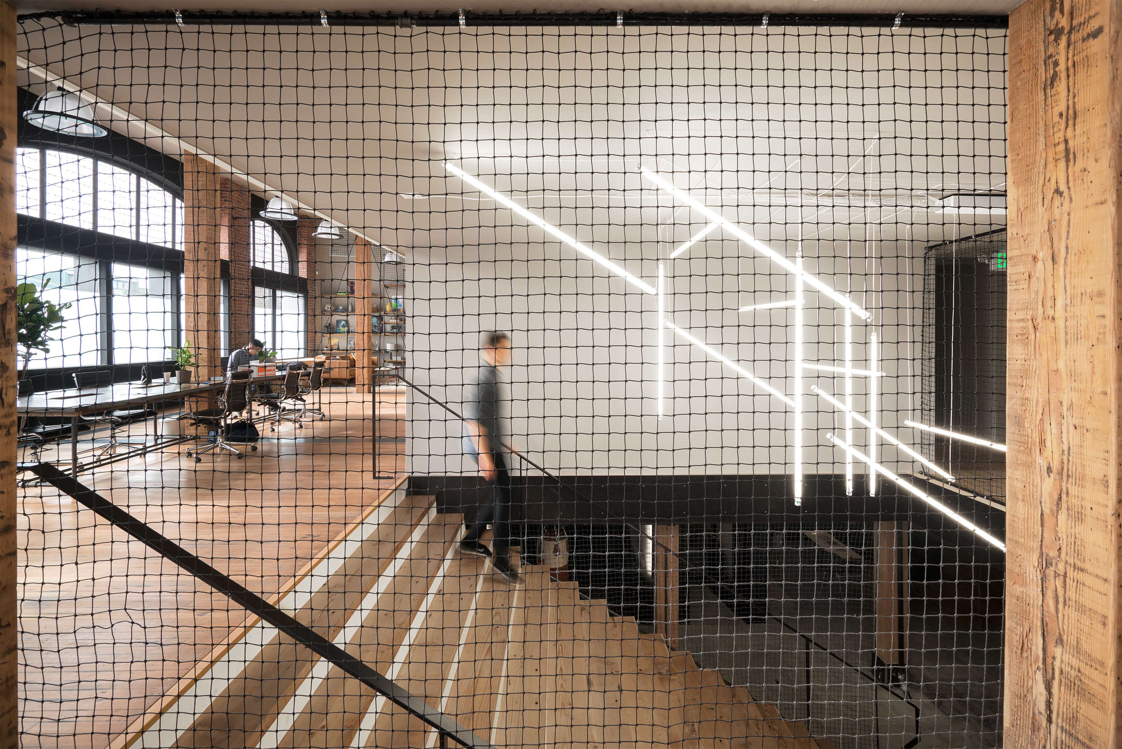 A person walks down a staircase in an open office space featuring modern lighting and wooden elements.