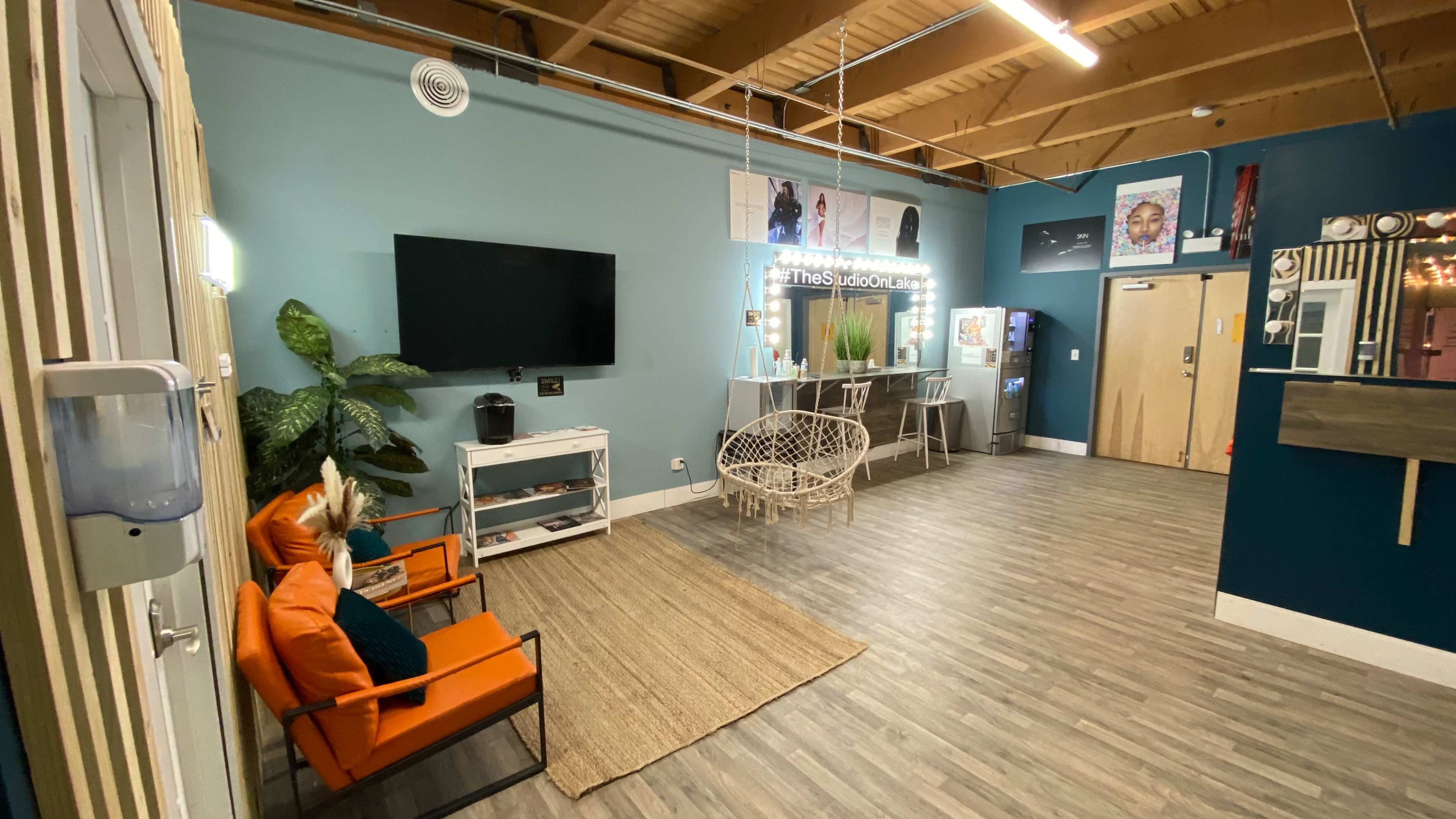 A spacious indoor area with a teal wall, a large television, a modern seating arrangement, a plant, and various decorations.