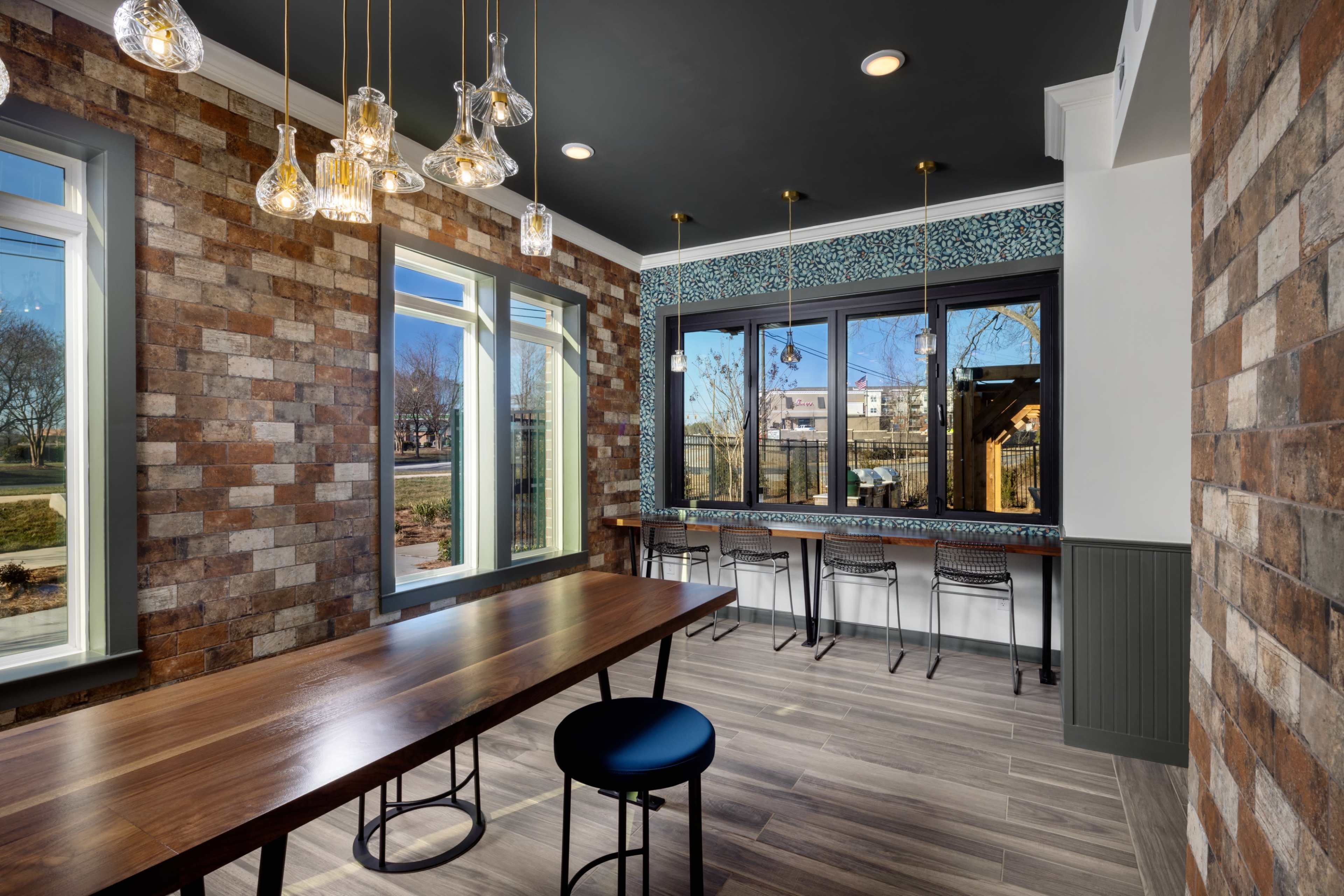 A modern room with a wooden table and barstools, surrounded by brick walls and large windows that let in natural light.