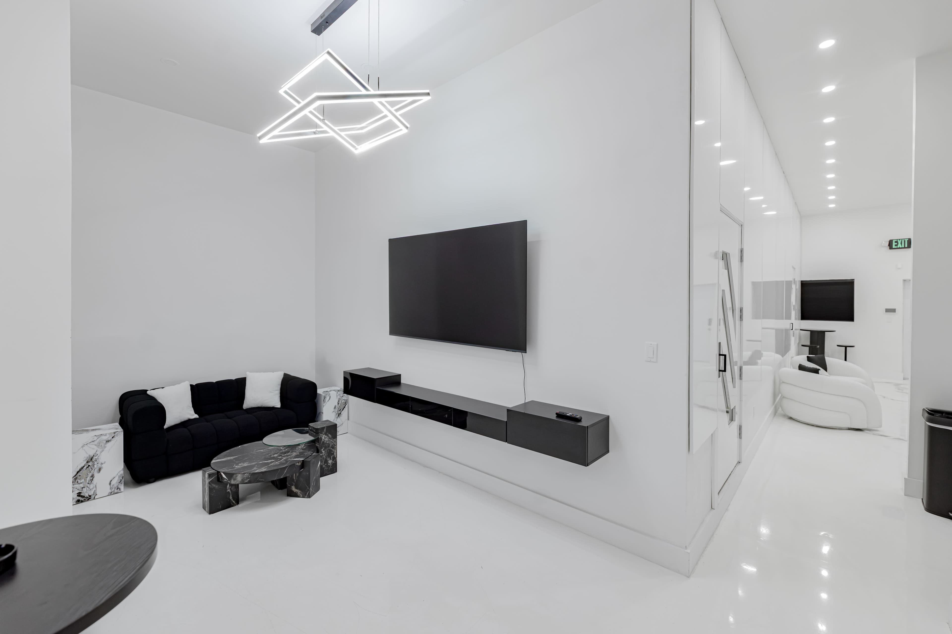 The image shows a modern, minimalist living space featuring a black sofa, a TV mounted on the wall, and a decorative table in a predominantly white environment.