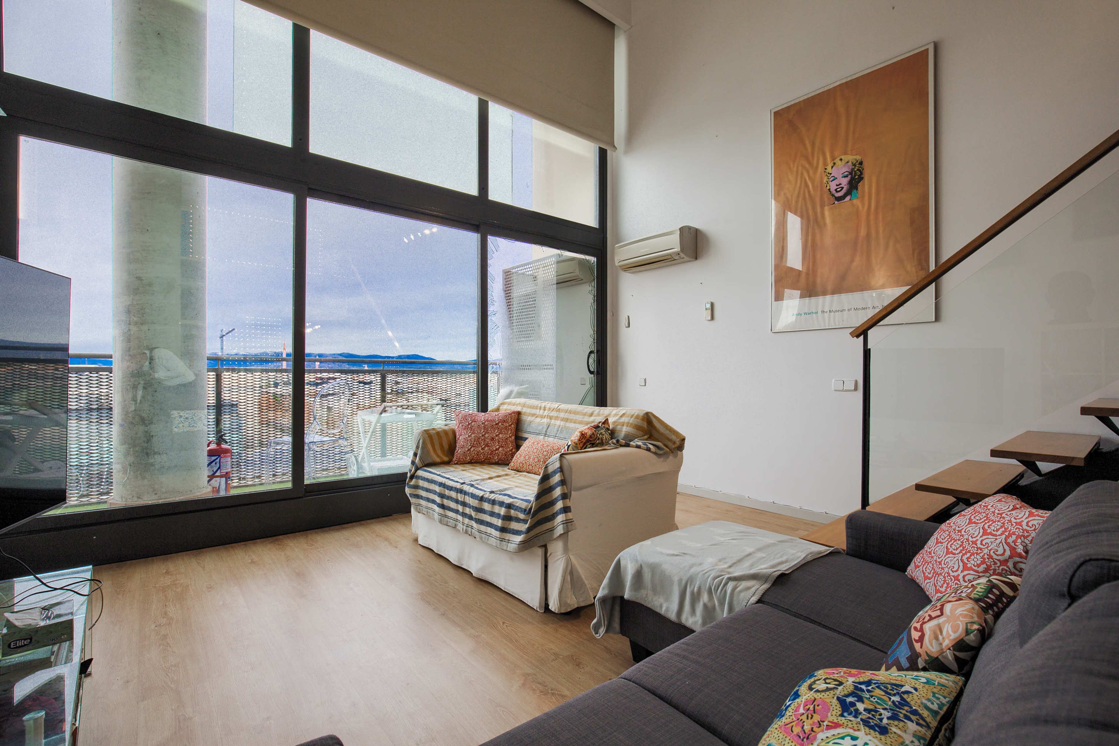 A modern living room features a couch, a chair with colorful cushions, and large windows overlooking a scenic view.