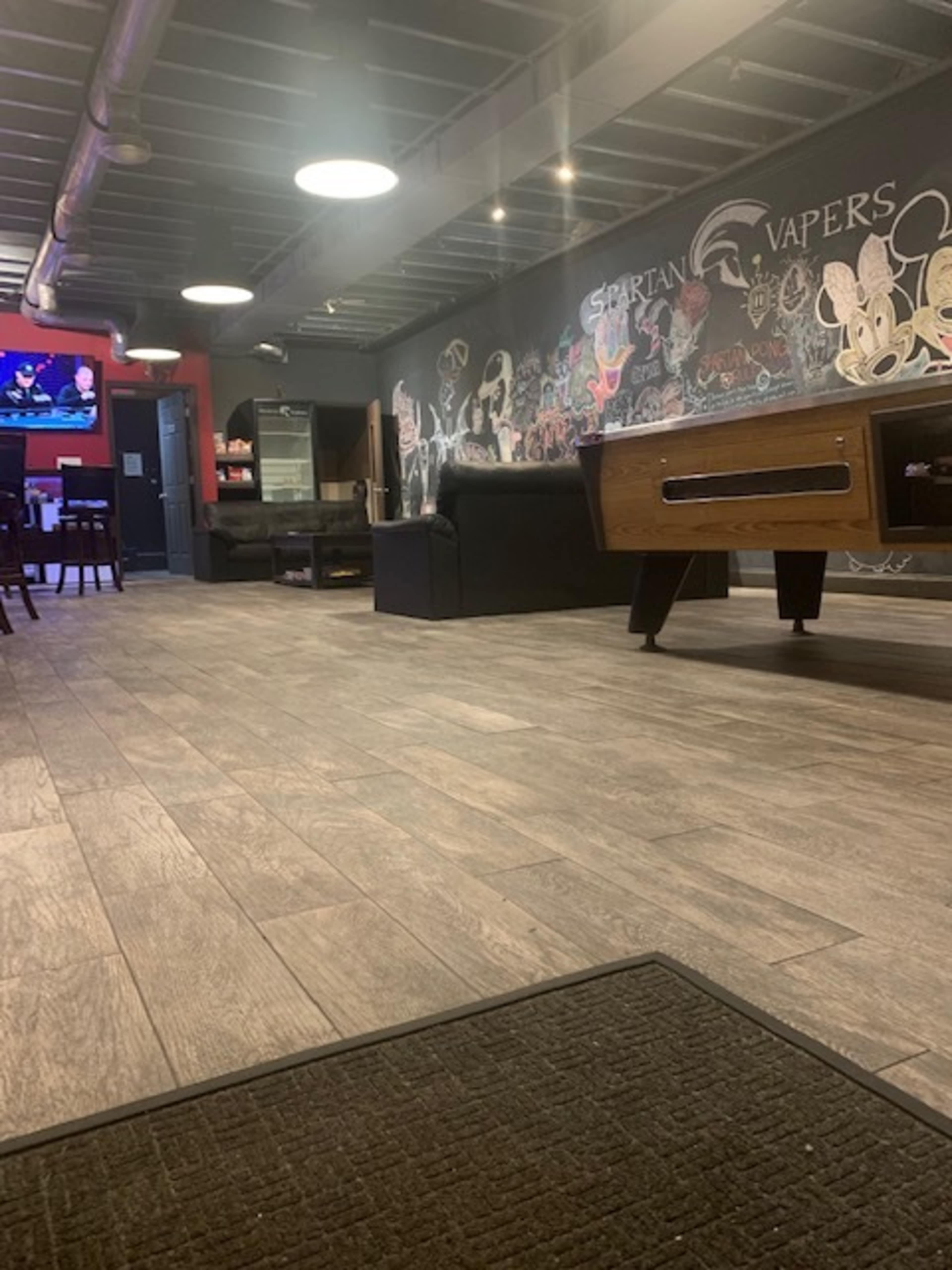 A modern lounge area with wooden flooring, a pool table, a chalkboard wall featuring colorful drawings, and a television mounted in the corner.