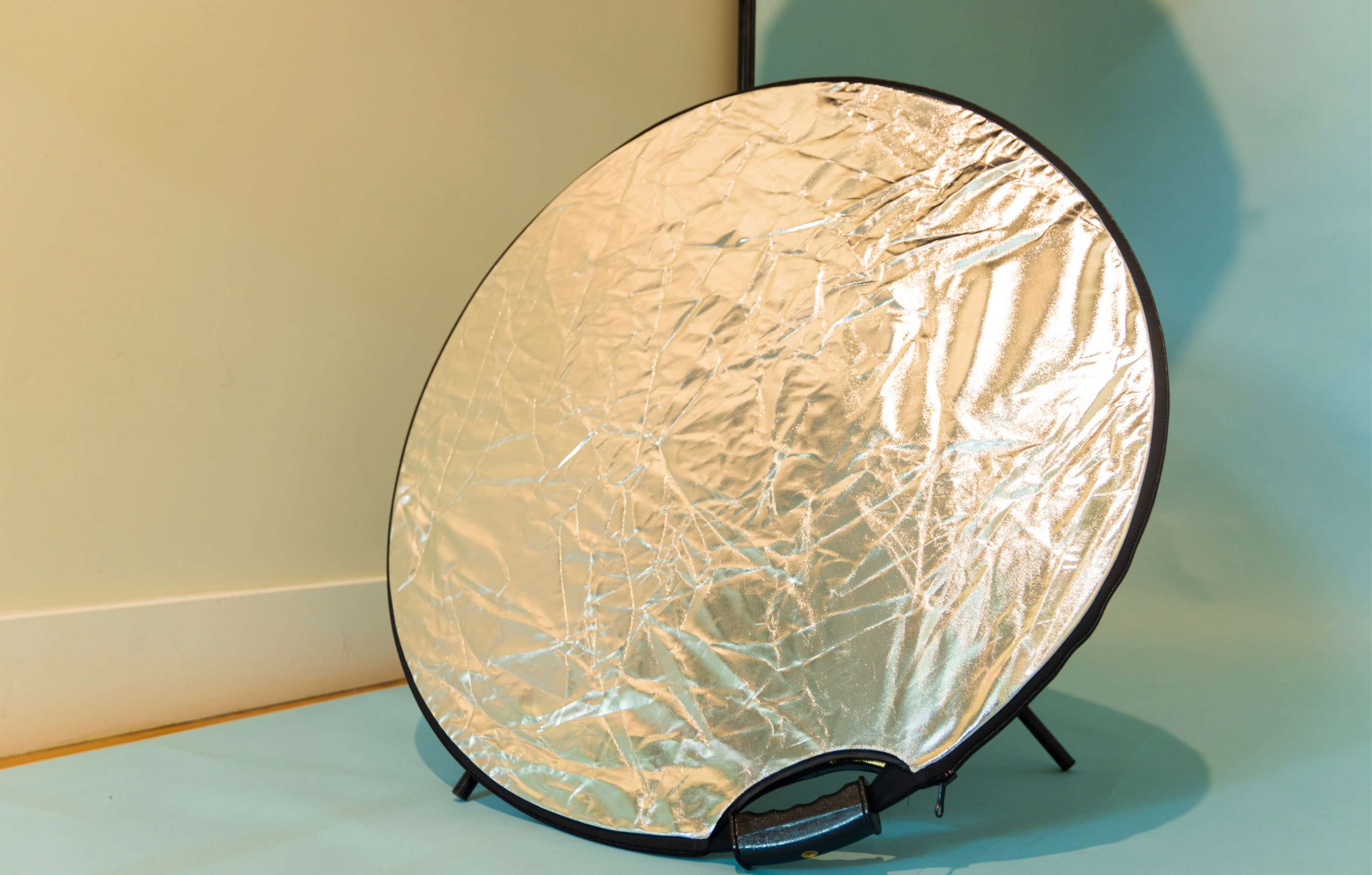 A round, silver reflector is positioned on a stand against a light blue background.