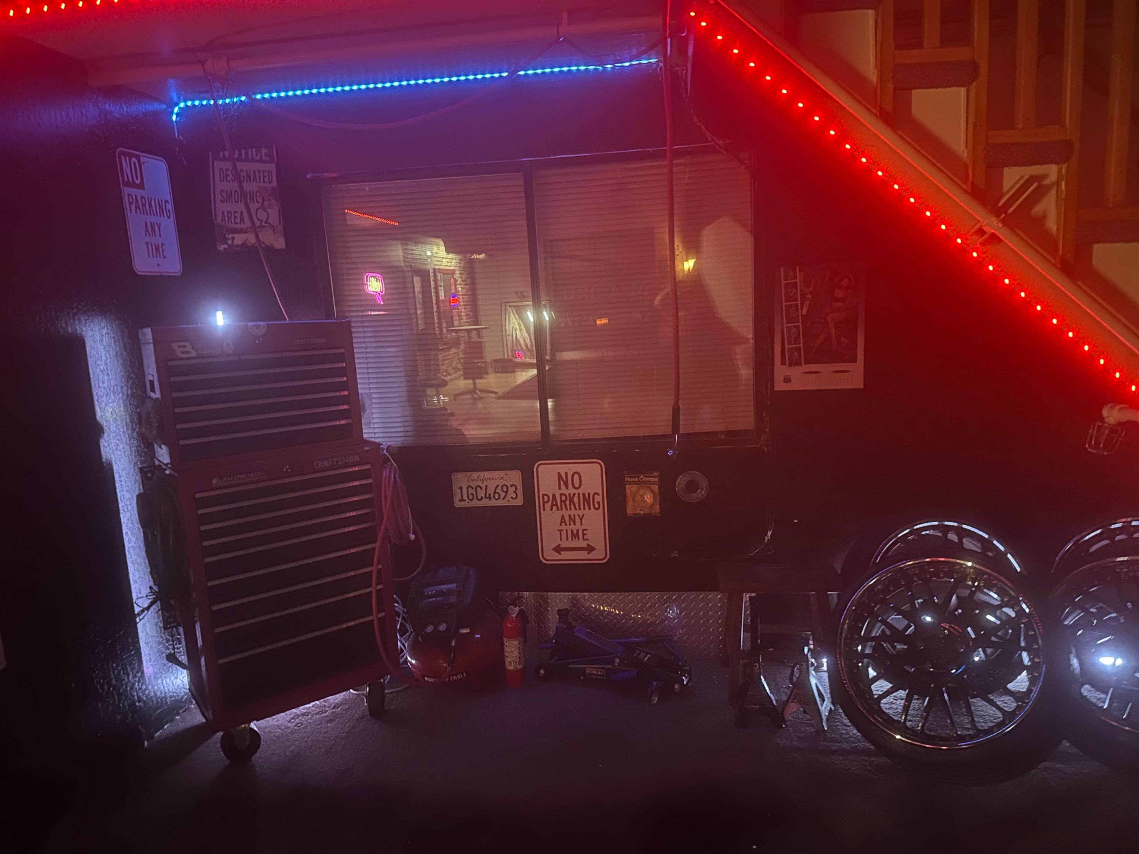 The image shows a dimly lit area with a tool chest, vehicle jack, large wheels, and various signs, including "NO PARKING ANY TIME."