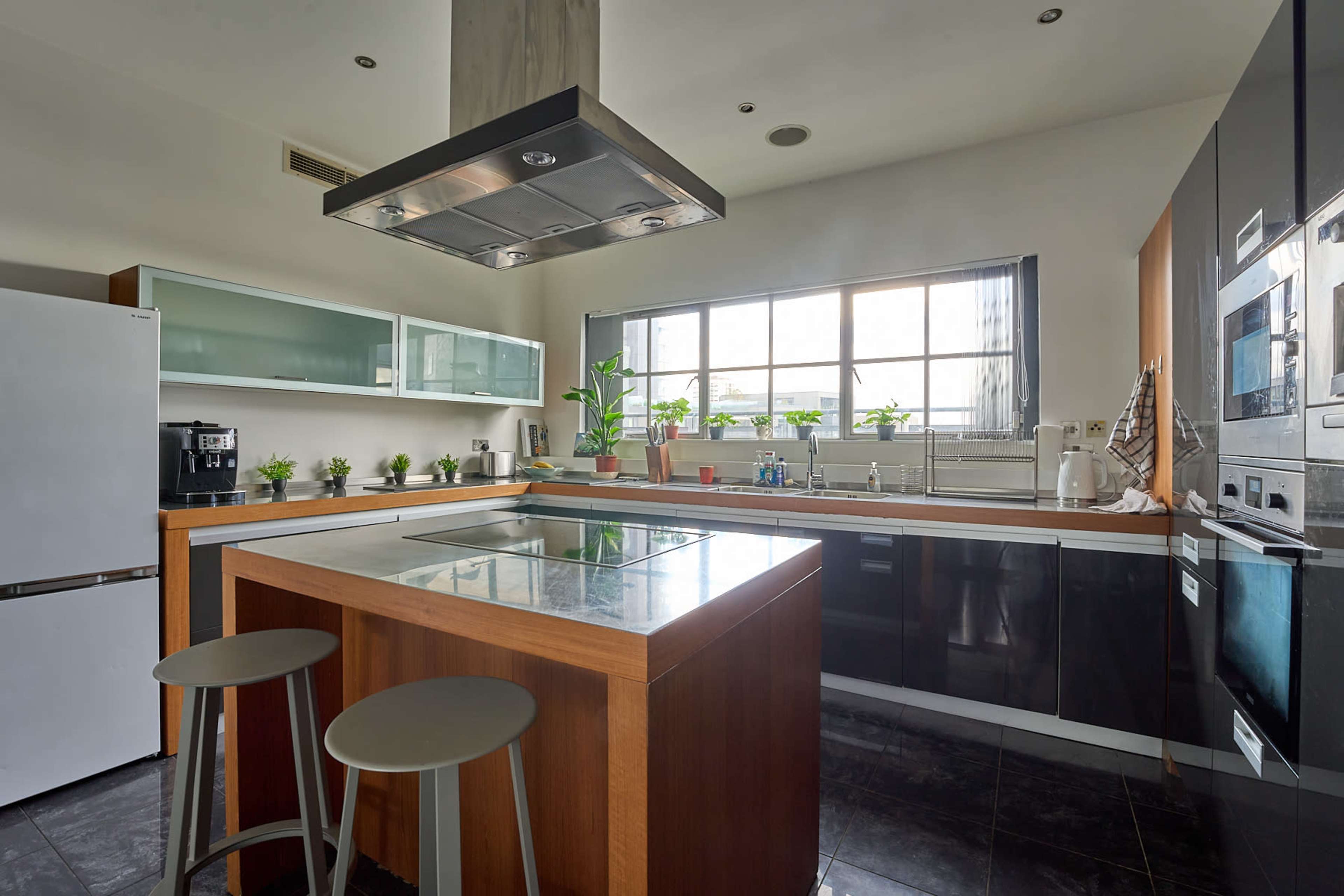 The image shows a modern kitchen with a central island, stainless steel appliances, and a large window allowing natural light to enter.