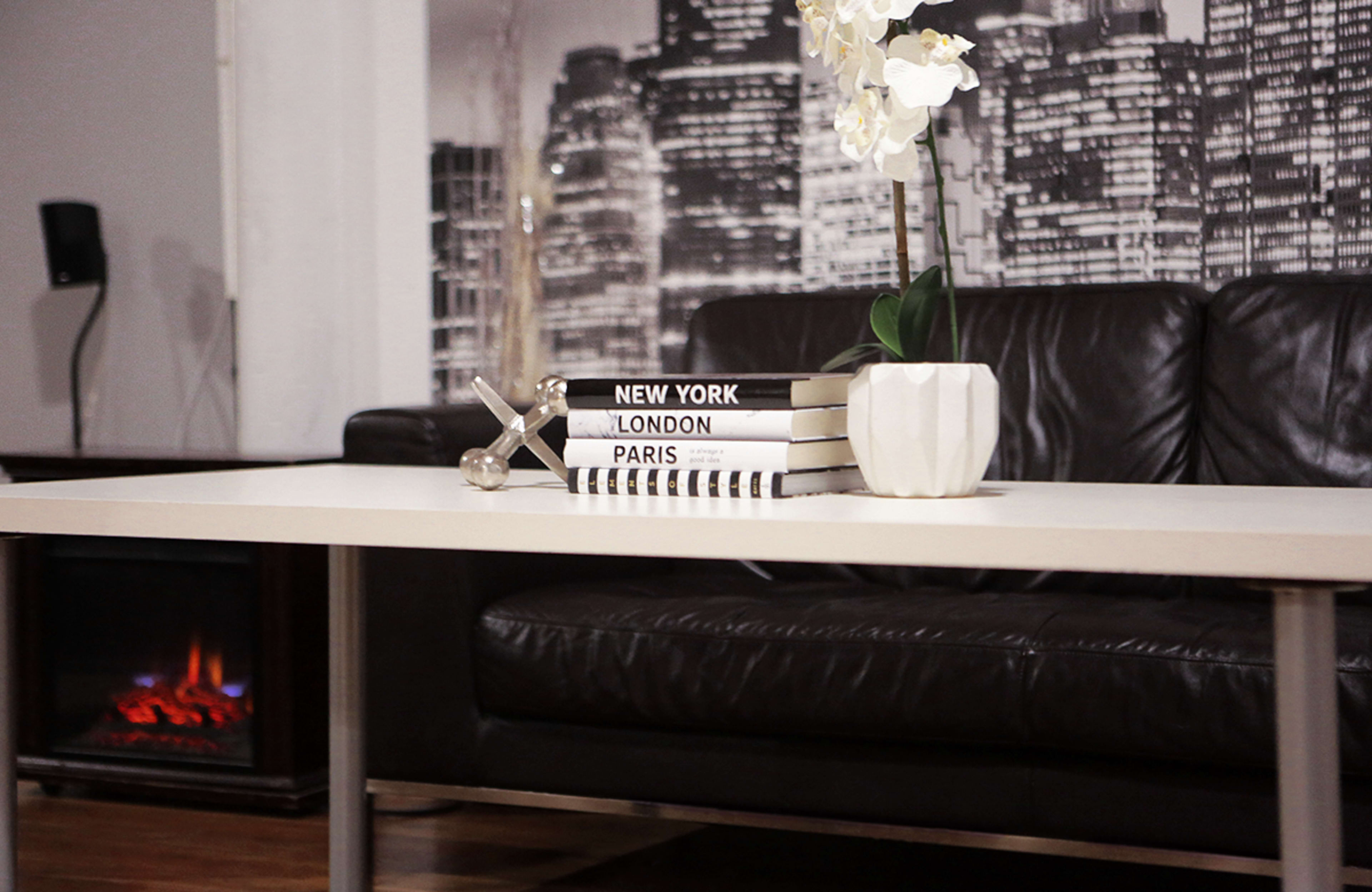 A coffee table with stacked books labeled "New York," "London," and "Paris," alongside a decorative vase with an orchid and a small sculpture.