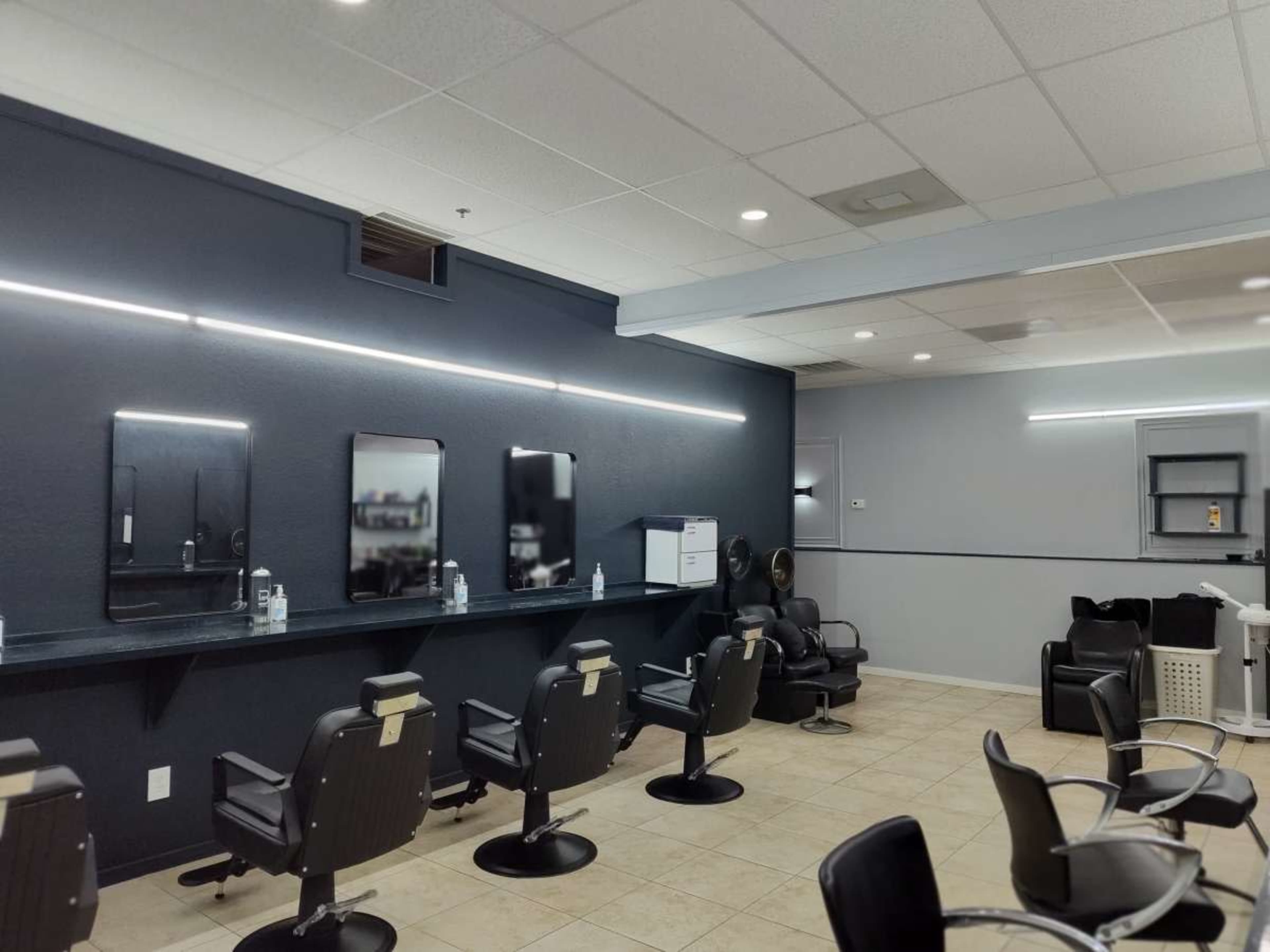 A modern hair salon features several styling stations with mirror reflections and black salon chairs arranged in a spacious layout.