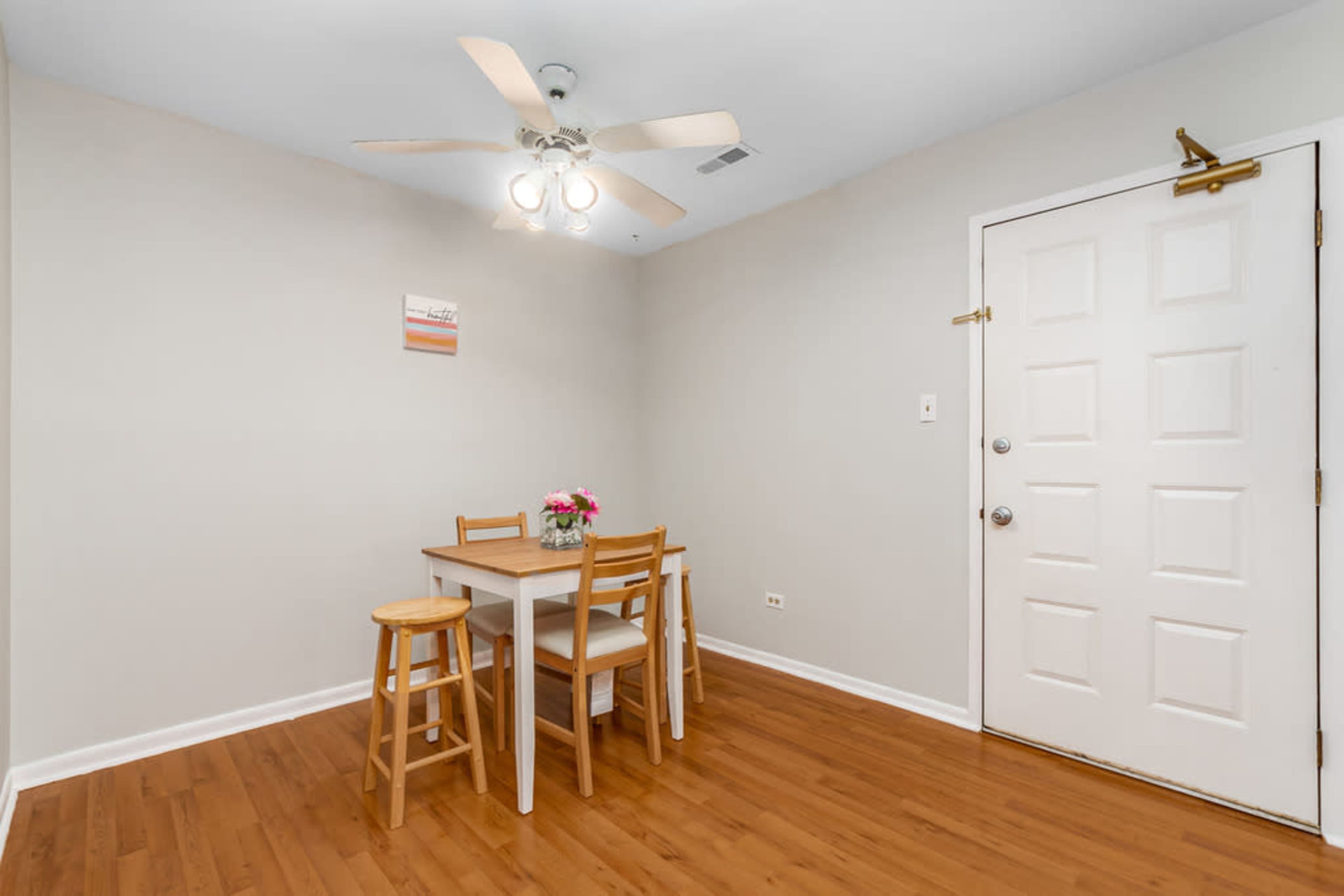 A small dining area features a table with four wooden chairs and a ceiling fan, adjacent to a door leading outside.