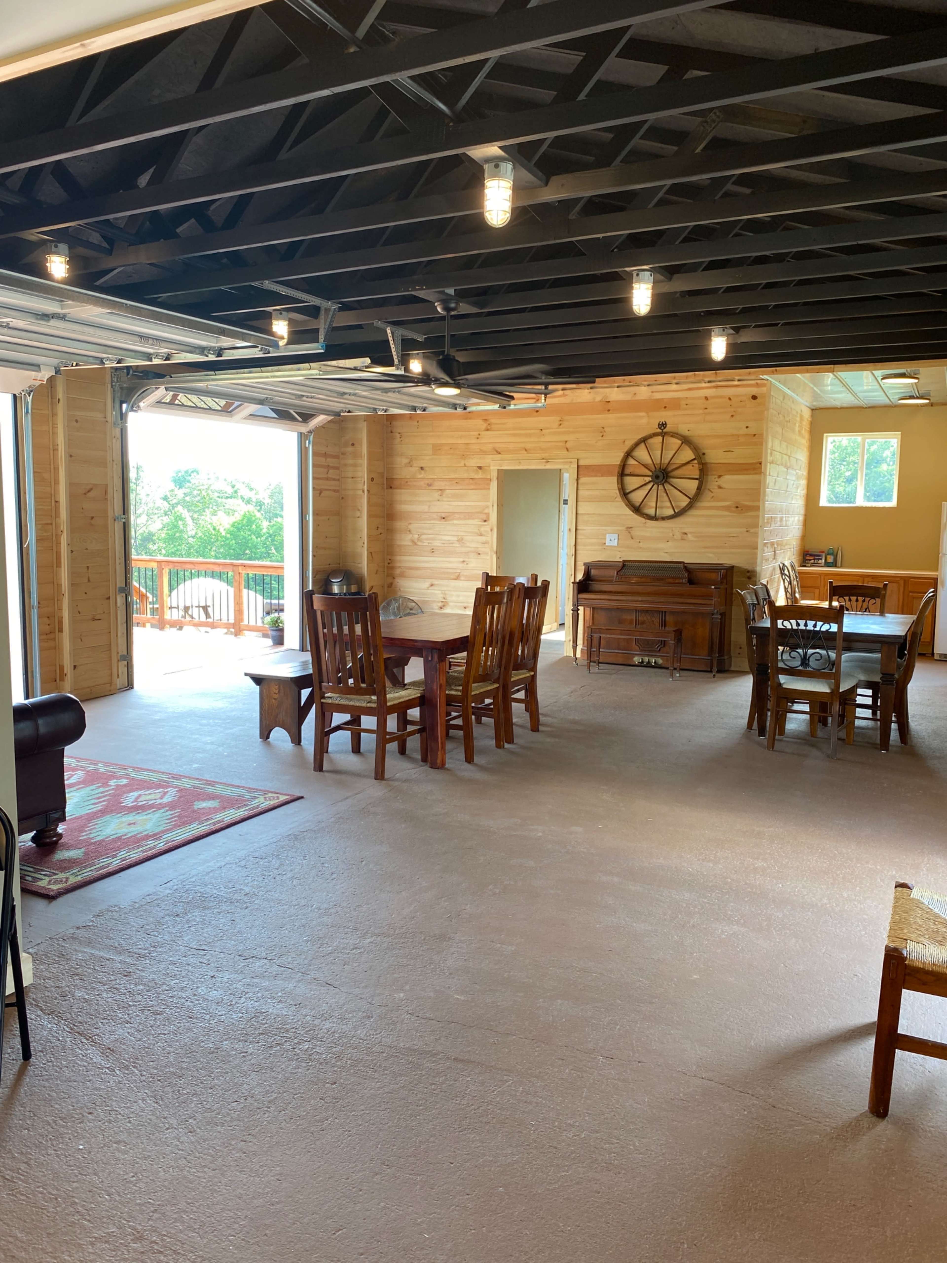 A spacious interior room featuring wooden dining furniture, a piano, and large windows that open to a view outside.