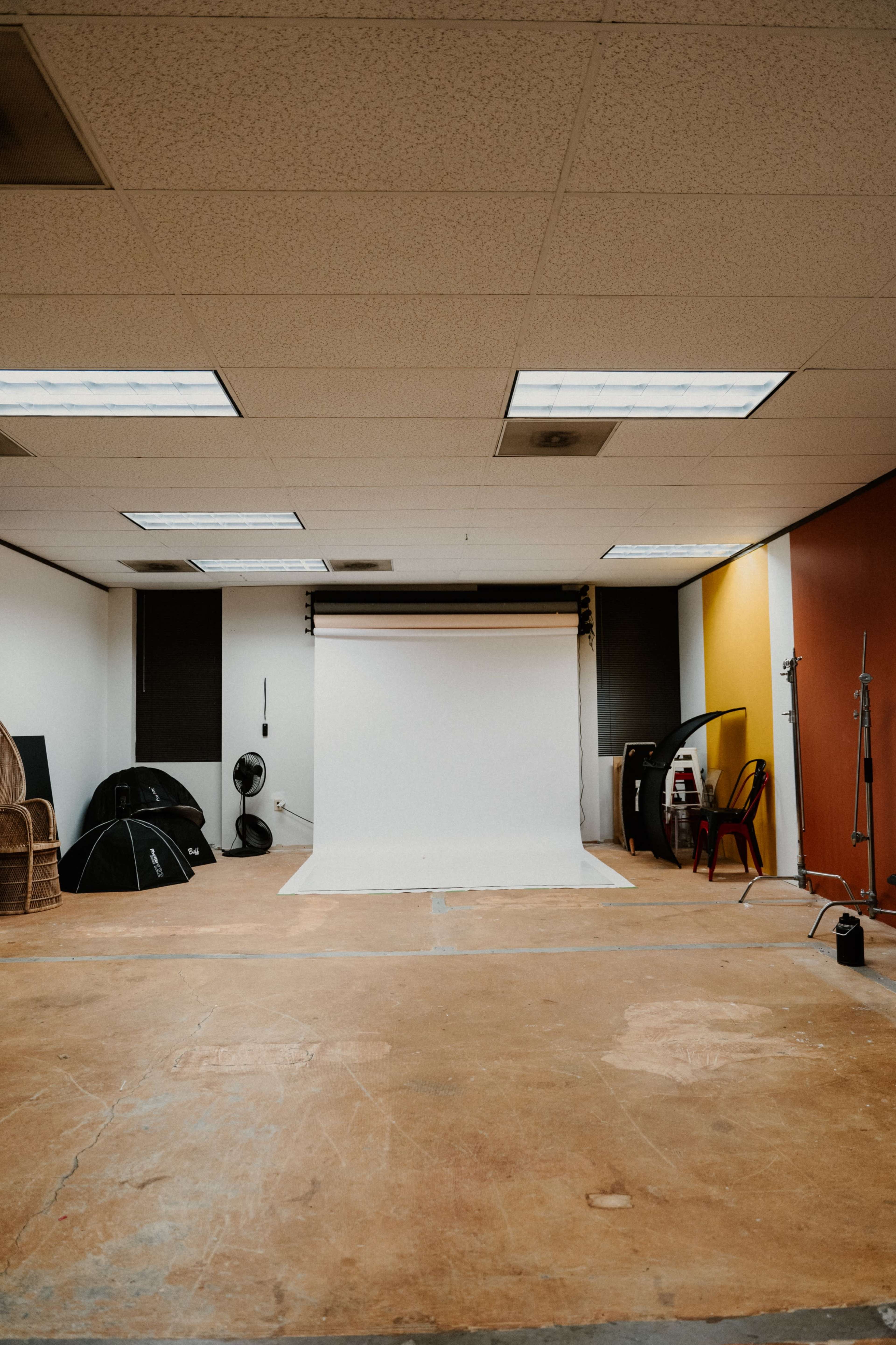 A spacious photography studio with a white backdrop, lighting equipment, and various props arranged against the walls.