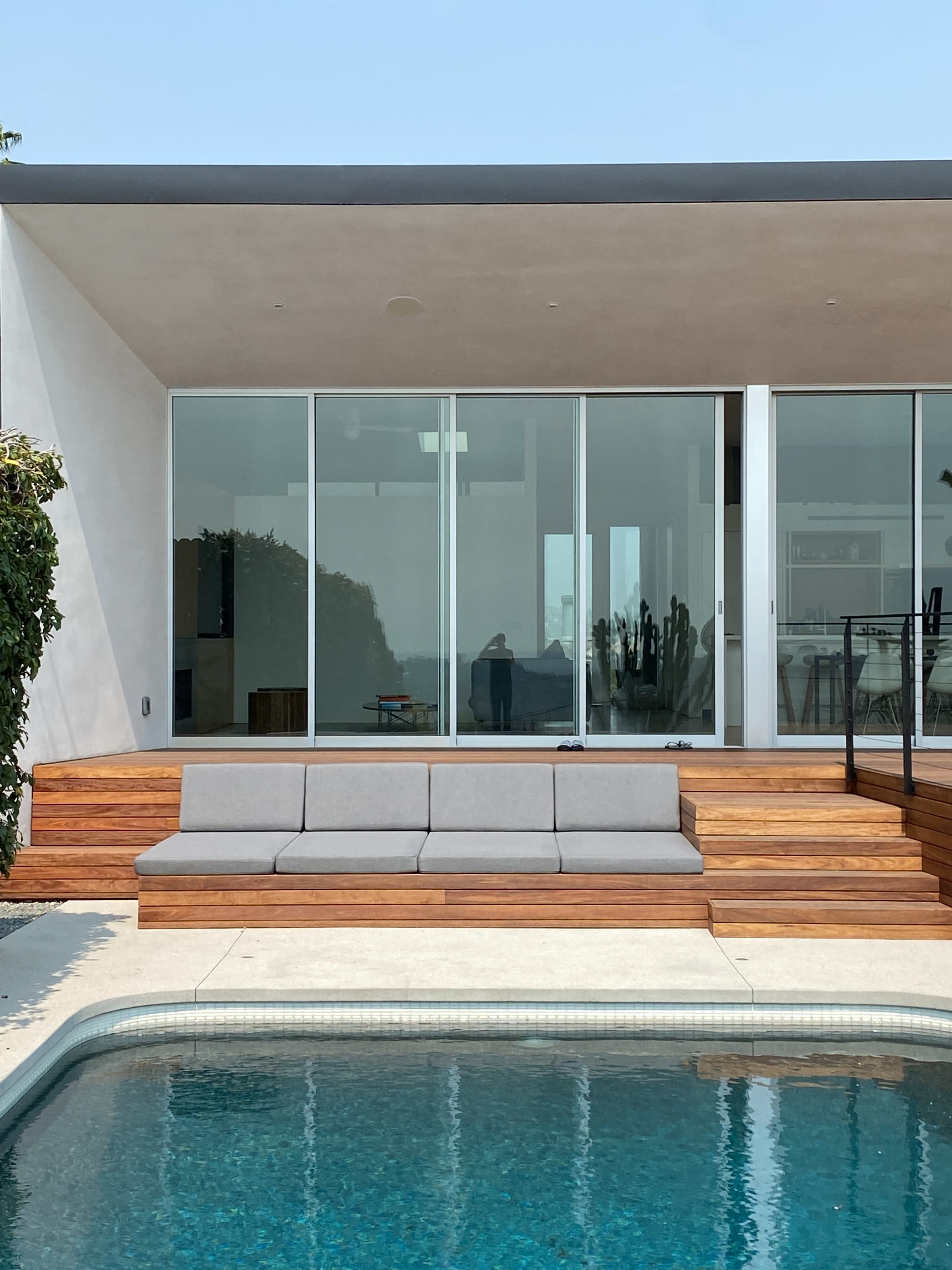 A modern house with large glass windows, a wooden deck, and a swimming pool in the foreground.