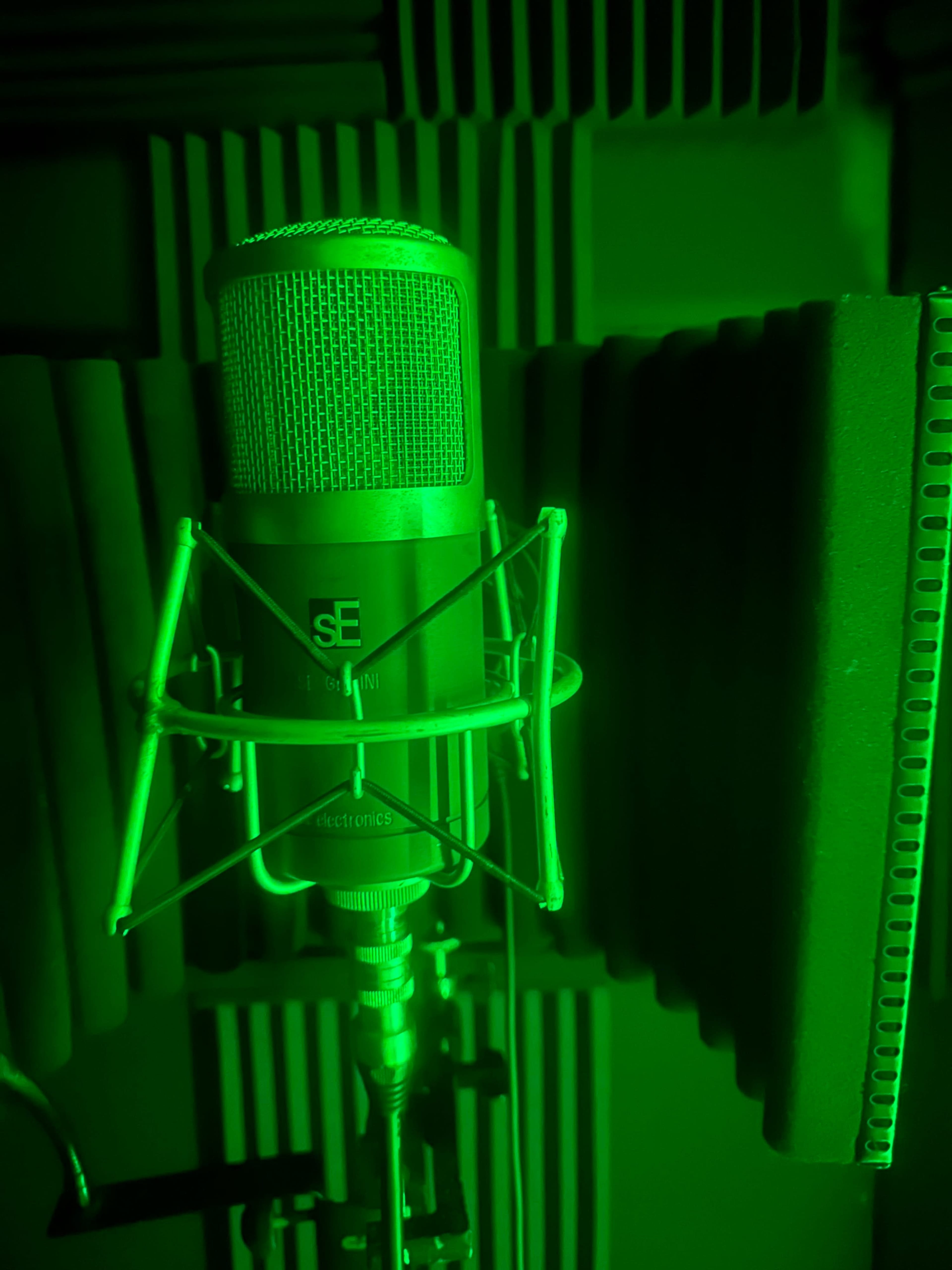A microphone is positioned in a soundproof booth with green lighting and acoustic panels in the background.