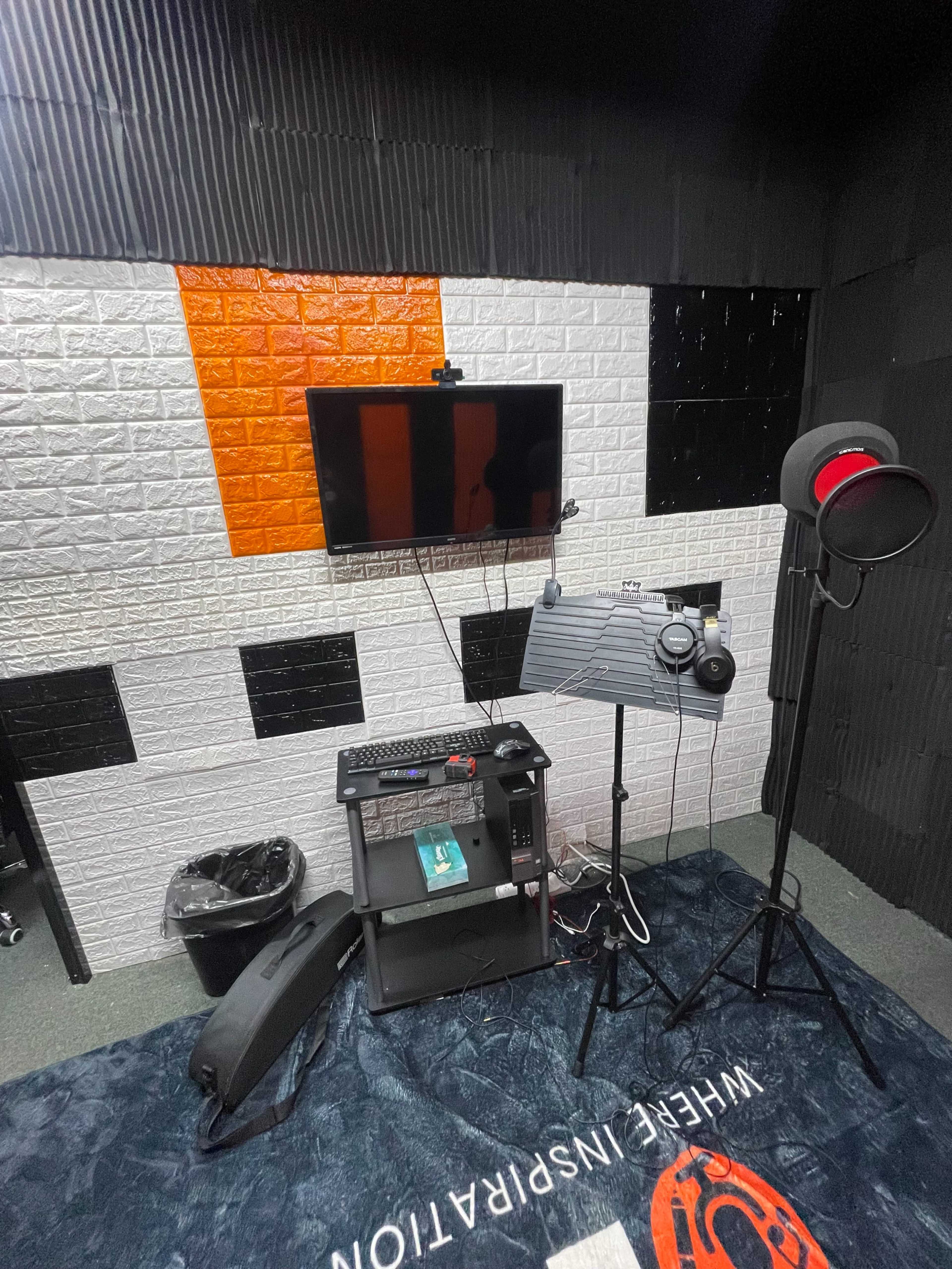 A recording studio equipped with a monitor, a microphone on a stand, a computer setup, and soundproofed walls.