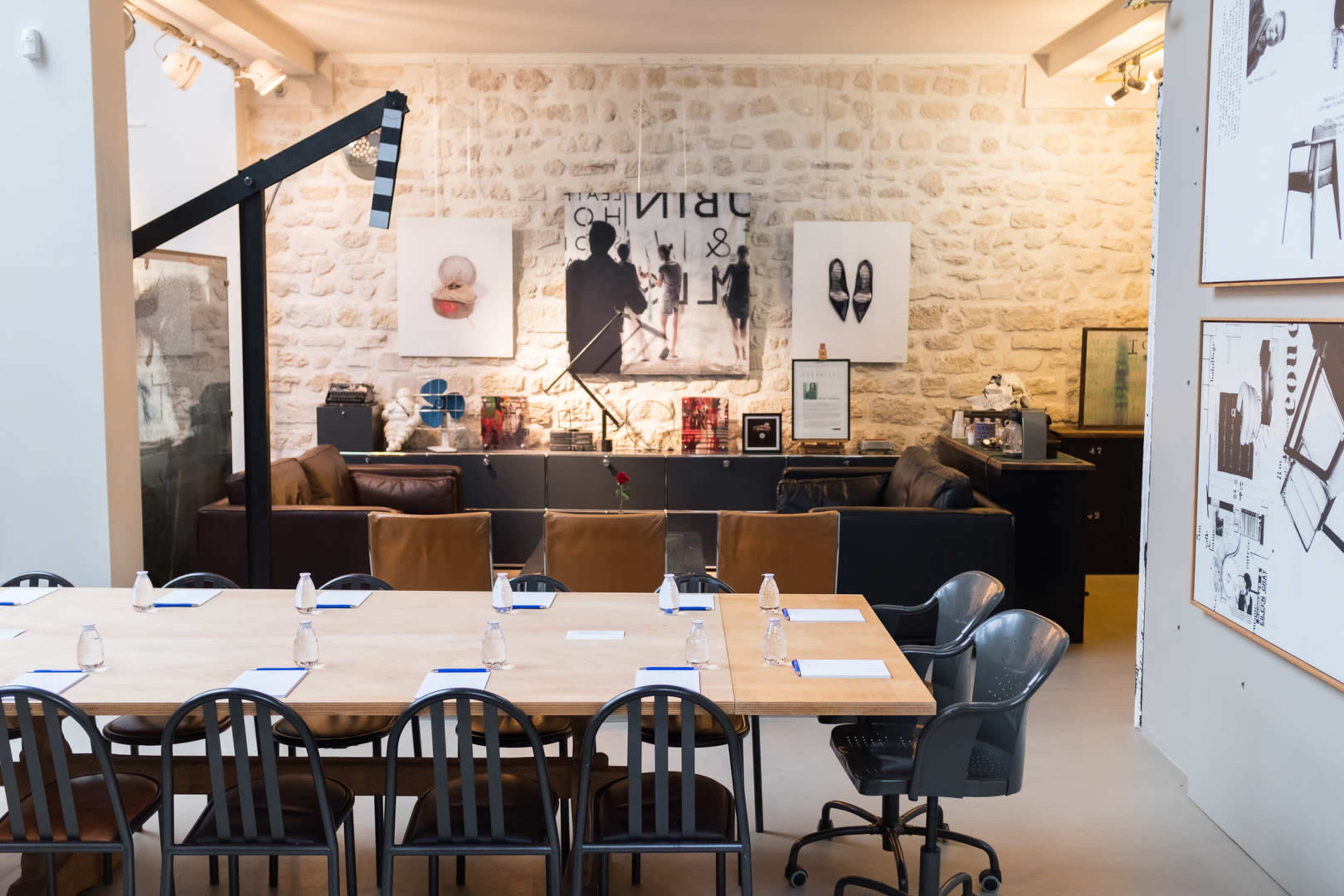 A modern meeting room features a long wooden table with chairs, surrounded by artworks and a stone wall in the background.
