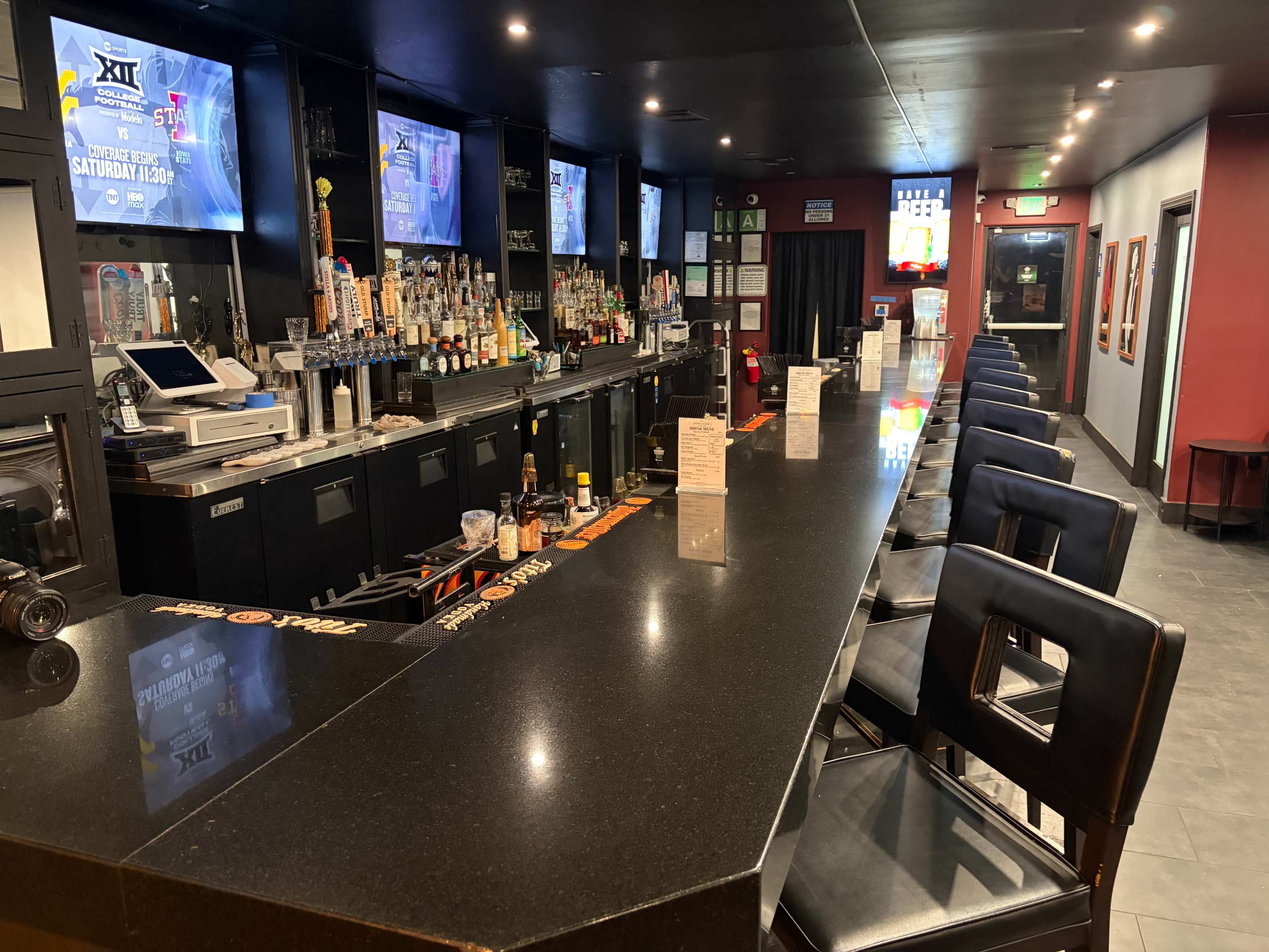 The image shows a modern bar with a long black countertop, multiple tap handles, and bar stools arranged neatly in front.