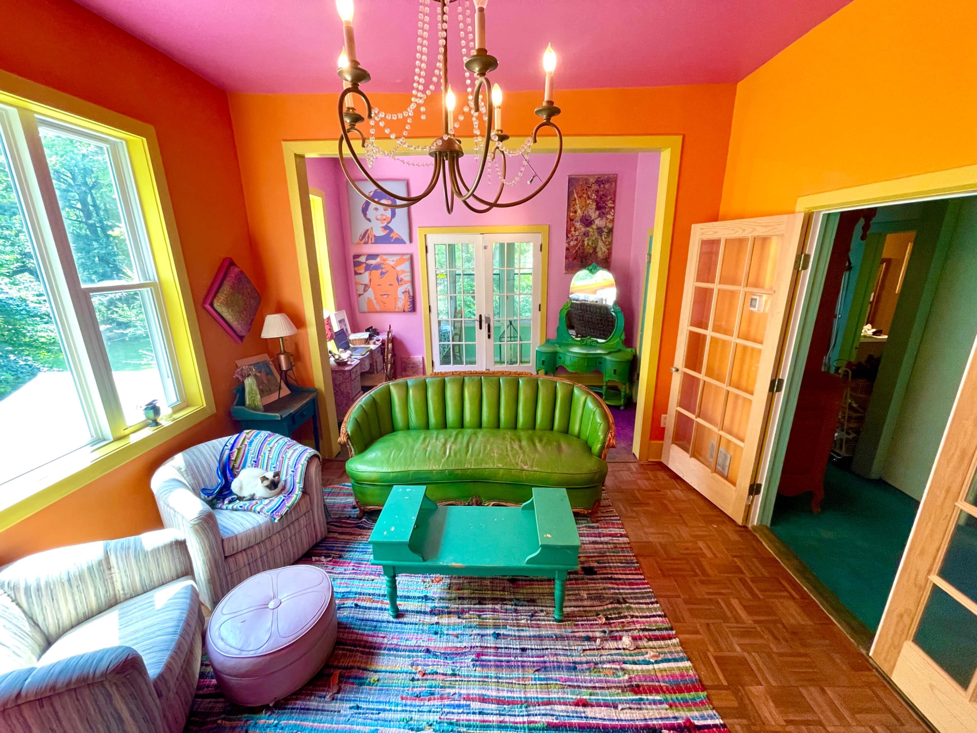The image showcases a brightly colored room with a green sofa, a striped chair, and a patterned rug, illuminated by a chandelier.