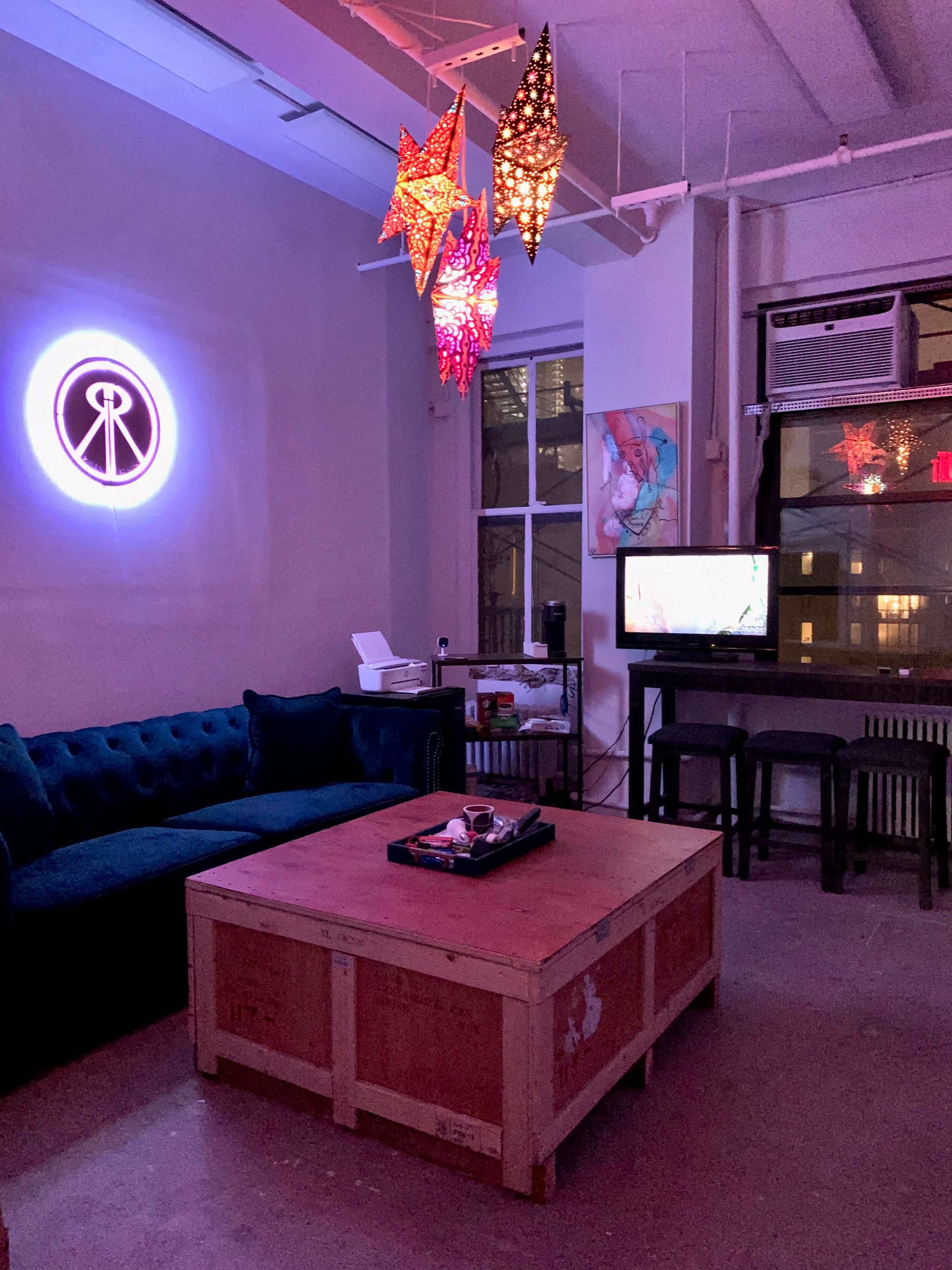 The image shows a dimly lit living room with a blue couch, a wooden coffee table, a television on a stand, and colorful star-shaped pendant lights hanging from the ceiling.