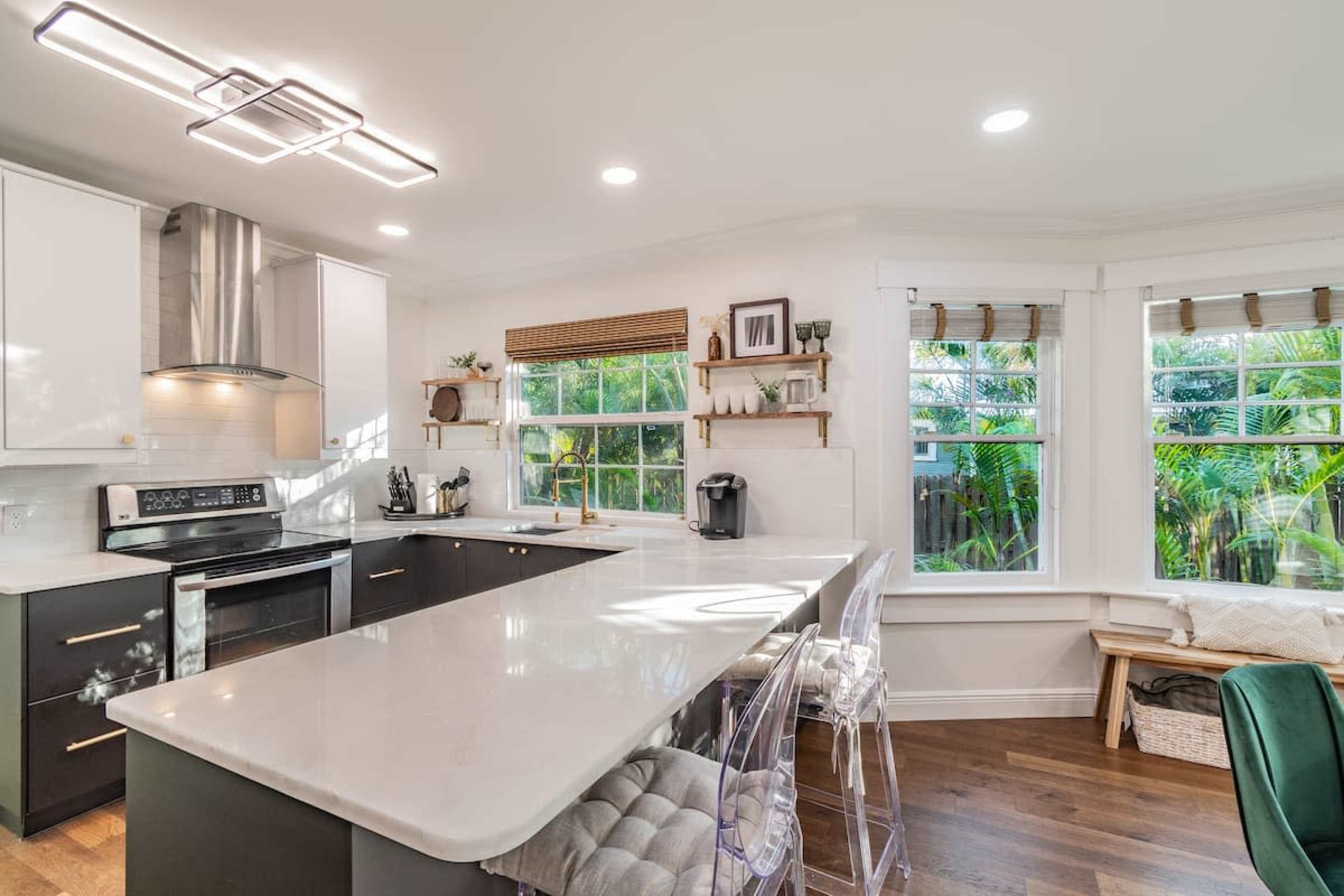 A modern kitchen featuring a large island, stainless steel appliances, and windows with a view of greenery outside.
