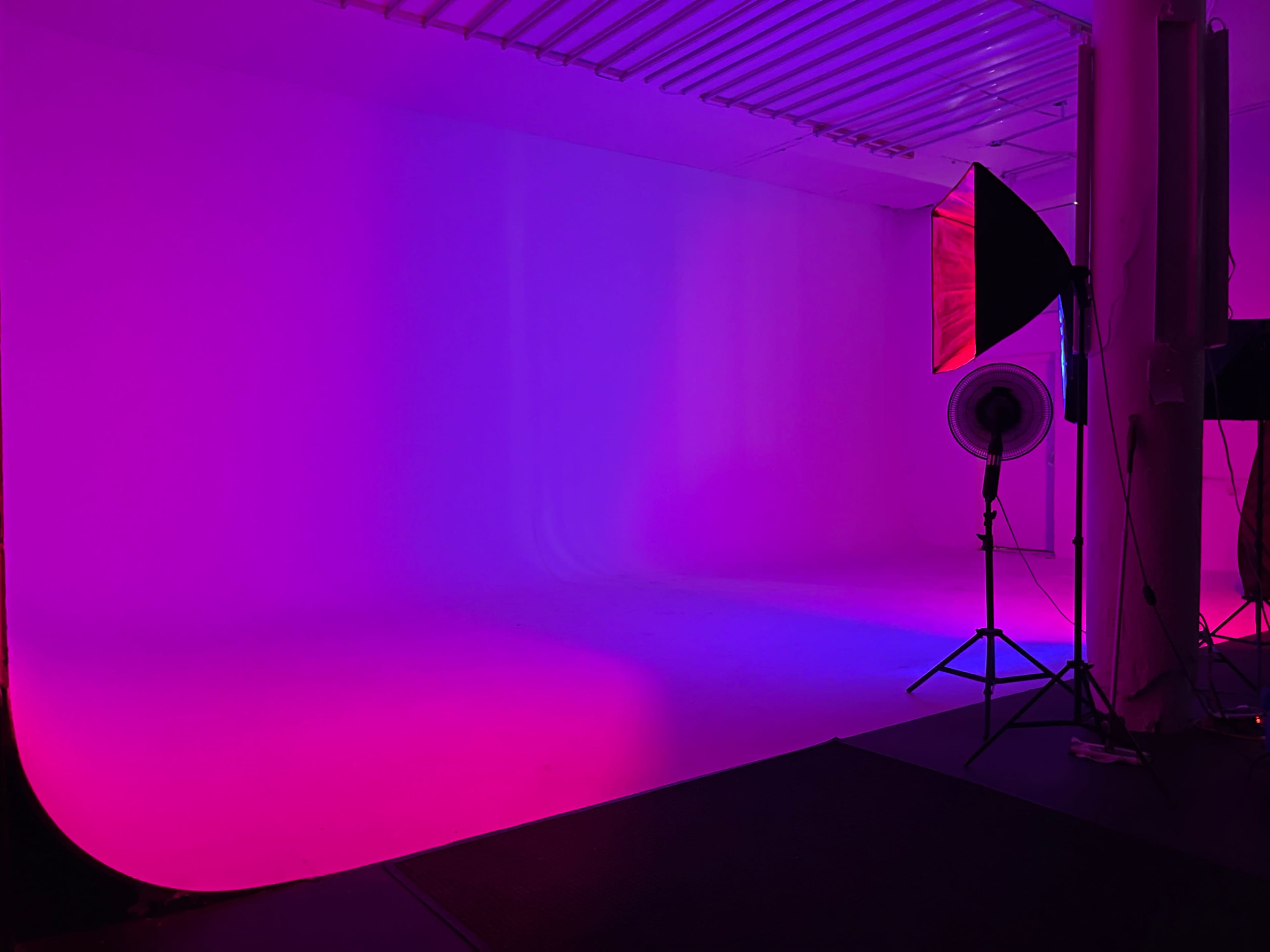 A photo studio with a brightly lit backdrop in shades of pink and purple, along with lighting equipment positioned on the side.