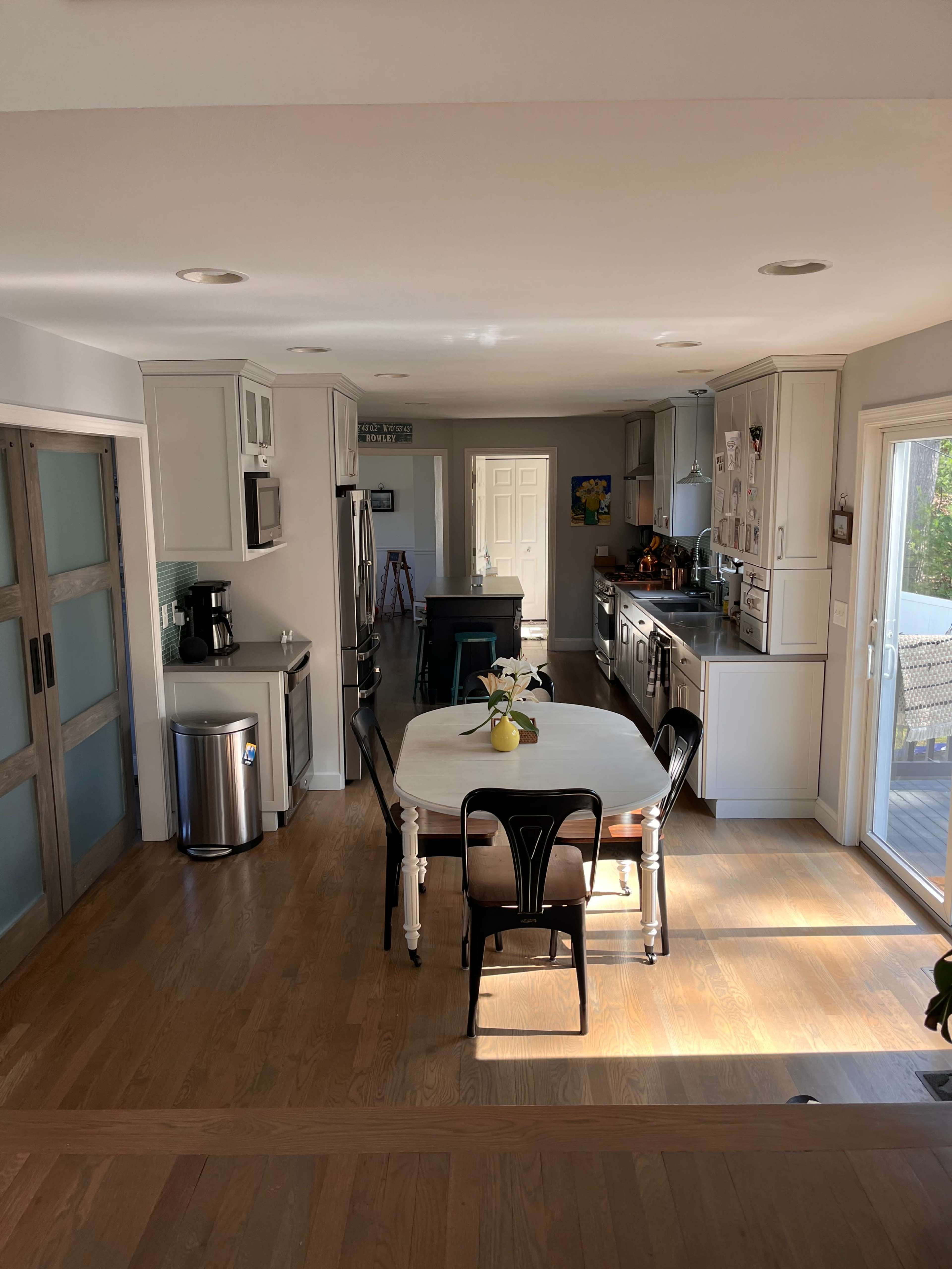 A modern kitchen with light-colored cabinets, a dining table at the center, and a stainless steel refrigerator.