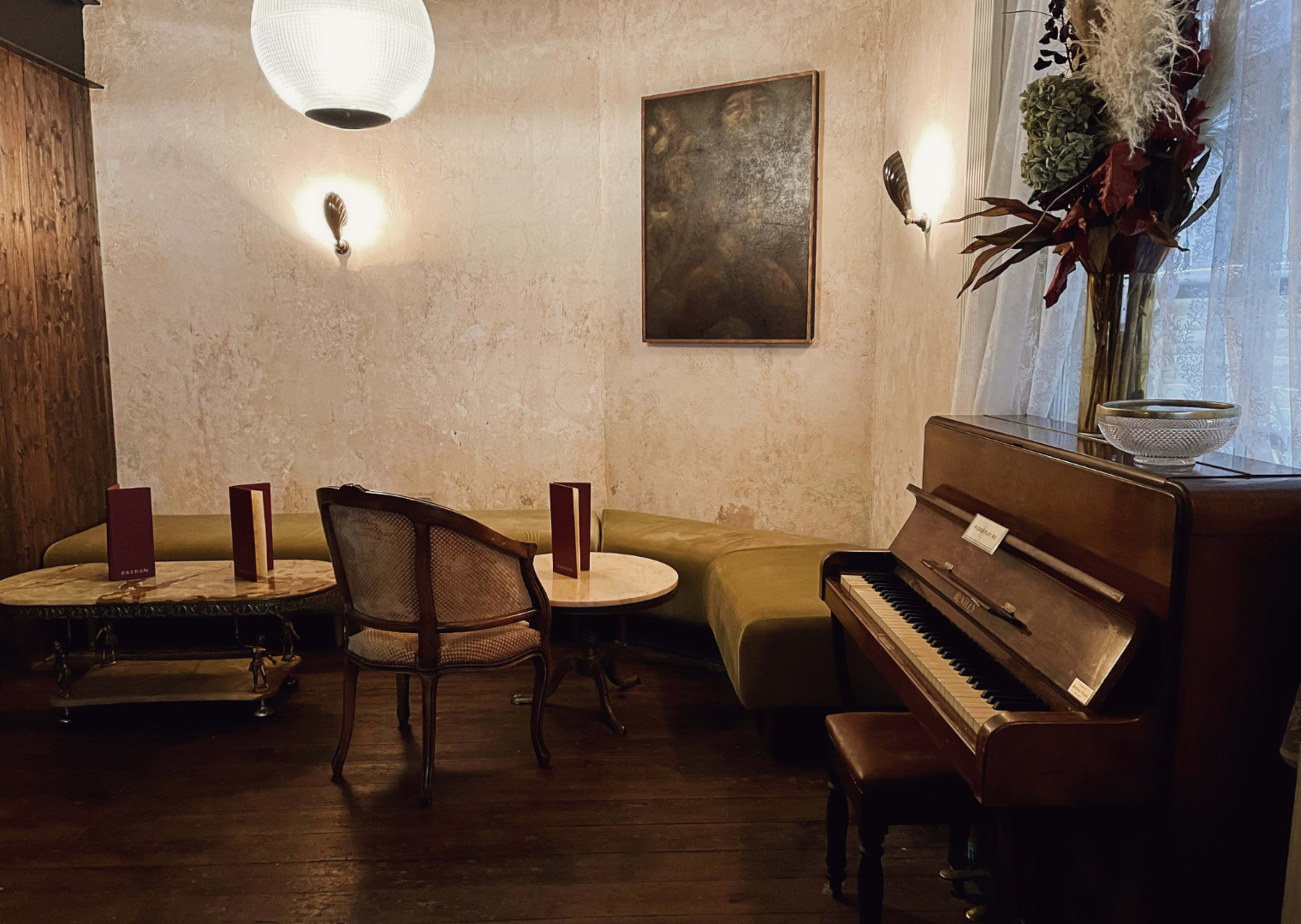 A cozy interior featuring a vintage piano, a small round table with chairs, and decorative wall art.