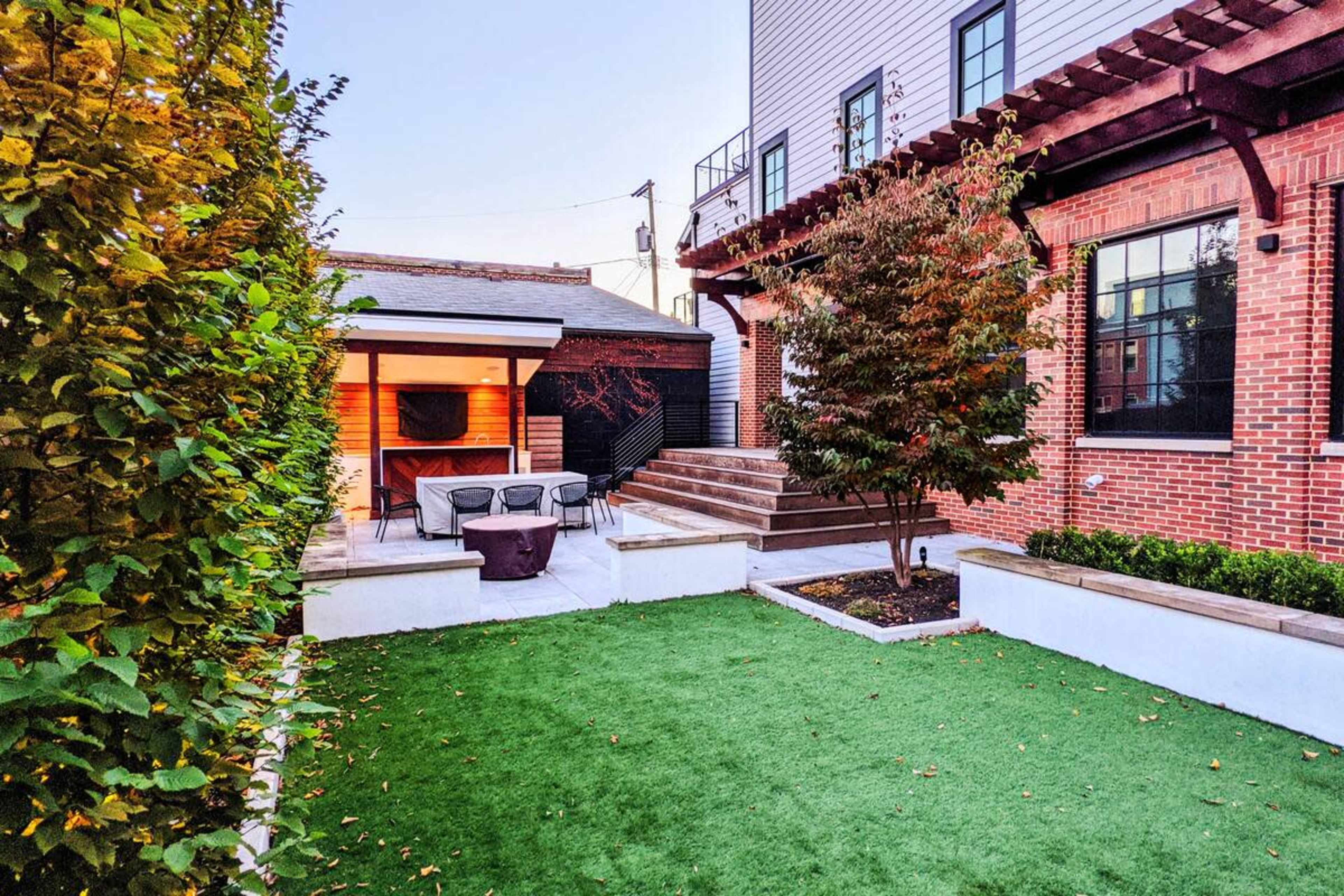 A well-maintained backyard featuring green grass, a patio with outdoor seating, and a landscaped area with trees and shrubs.