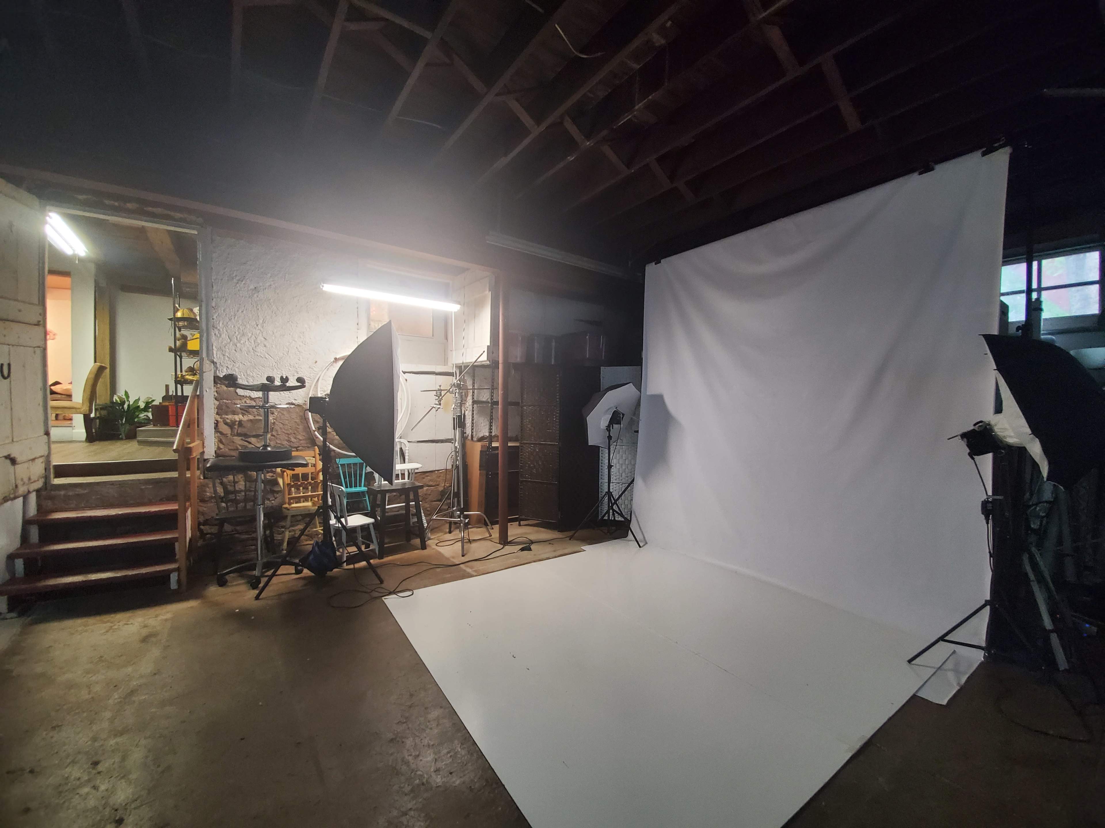 A photo studio setup featuring a white backdrop, lighting equipment, and a staircase leading to a different area.