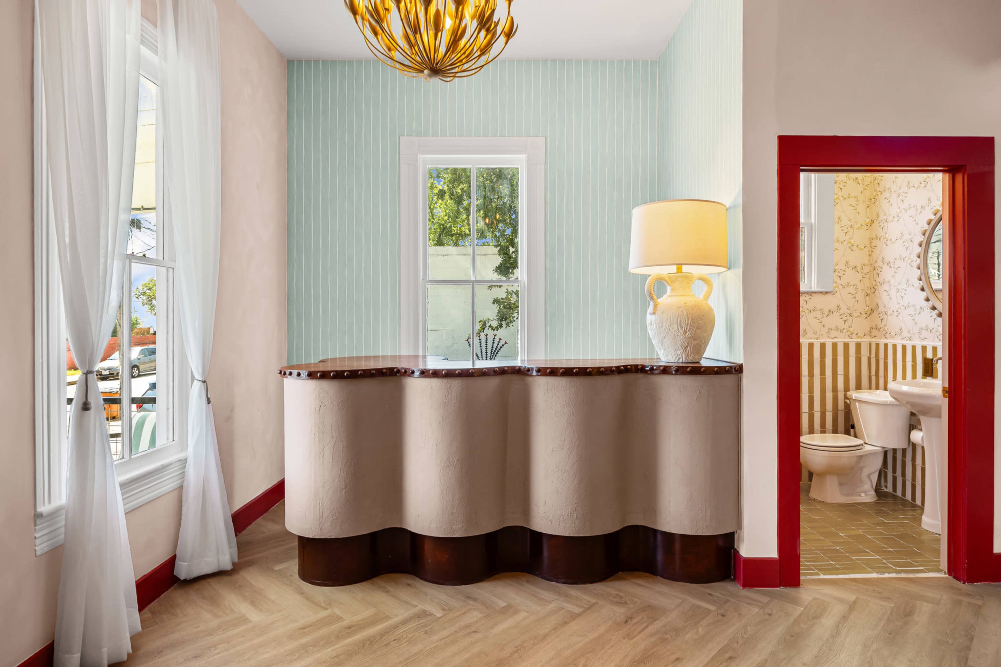 The image shows a brightly lit reception area with a curvy wooden front desk and a small bathroom visible through an open door.