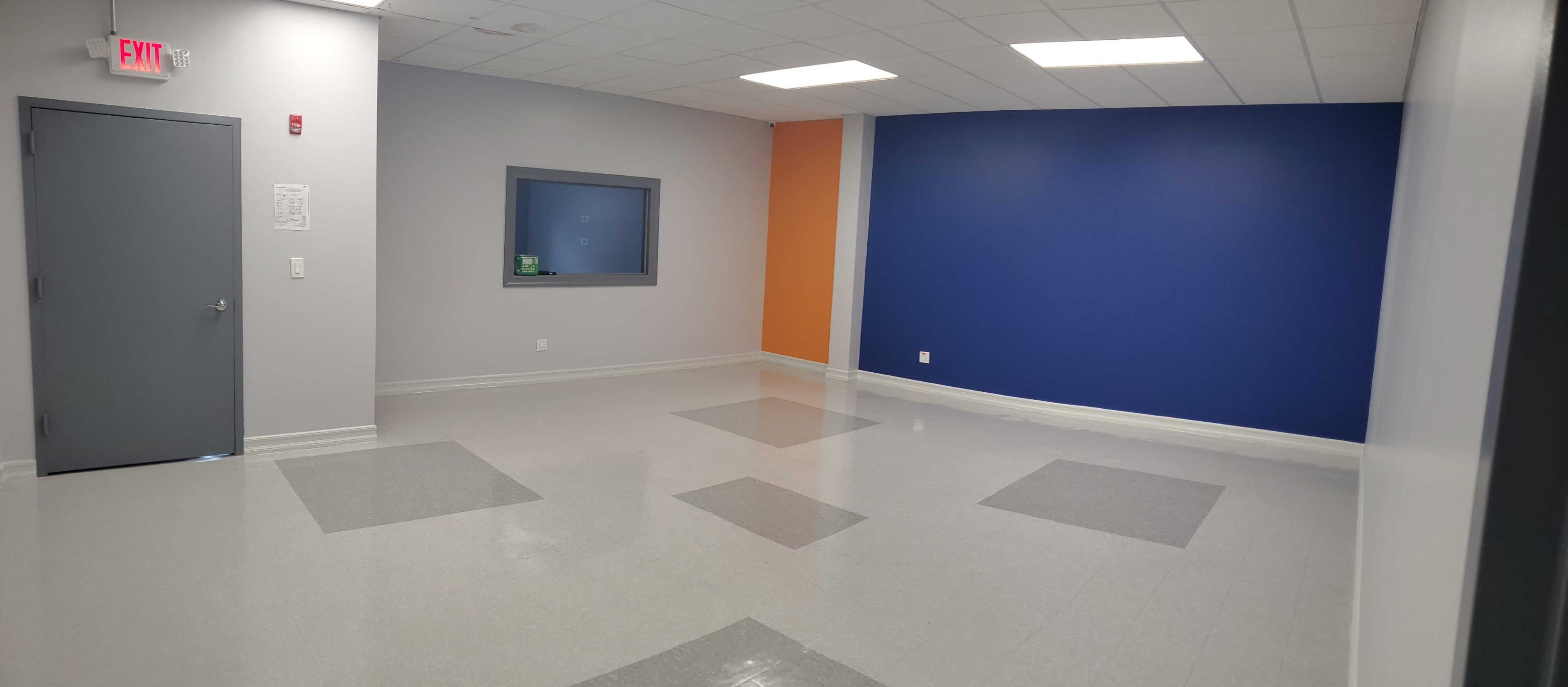 The image shows an empty room with gray and blue walls, a window on one side, and a polished floor with square tiles.