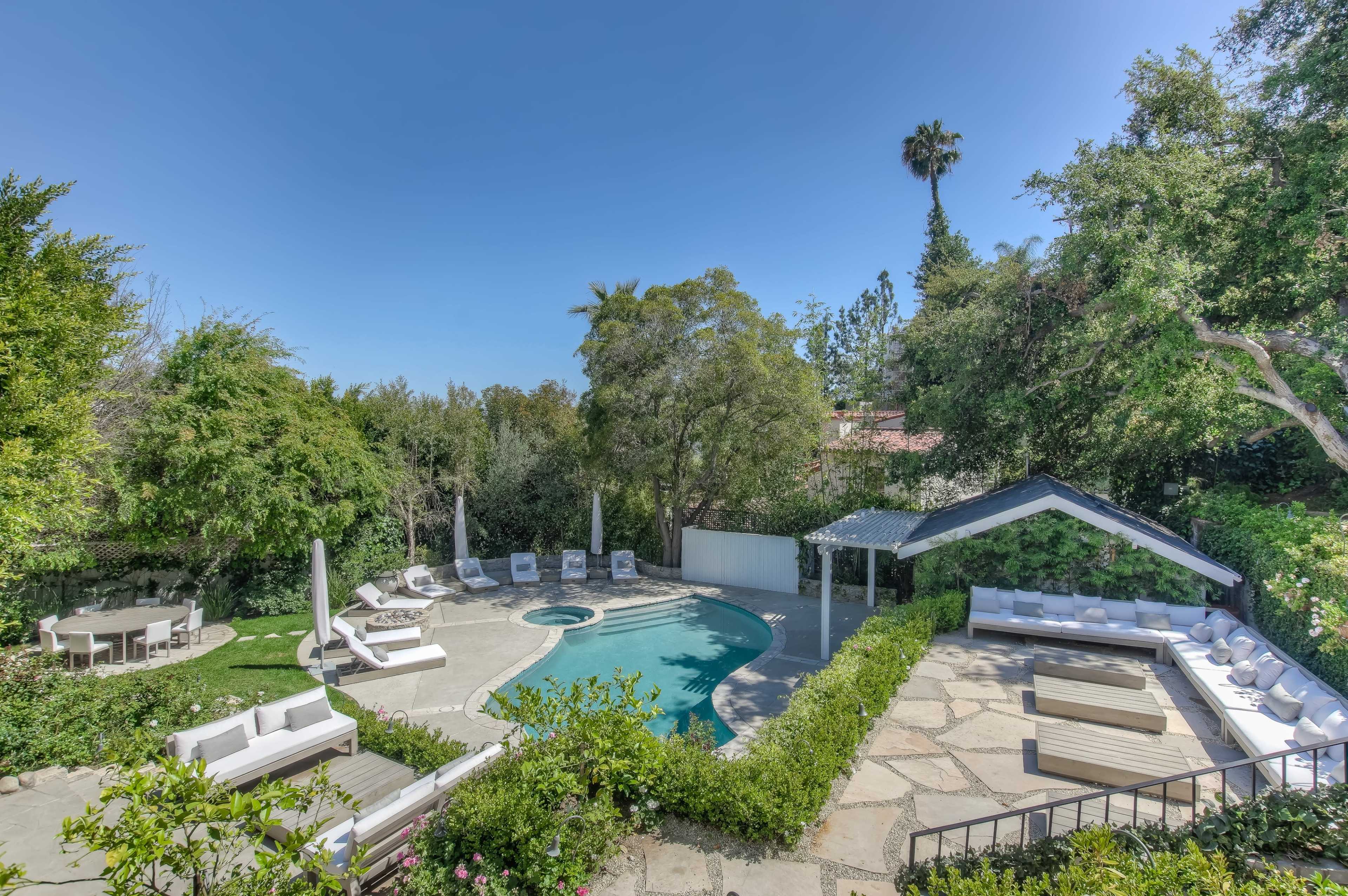 A landscaped outdoor space featuring a swimming pool, lounge chairs, and a covered seating area surrounded by greenery.